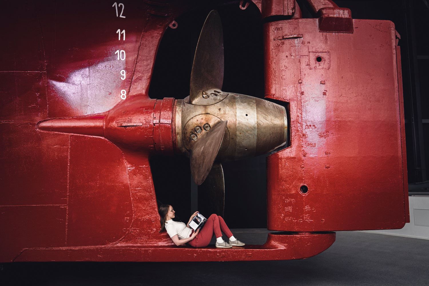 Jente sitter under propellen på MS Finnmarken og leser bok