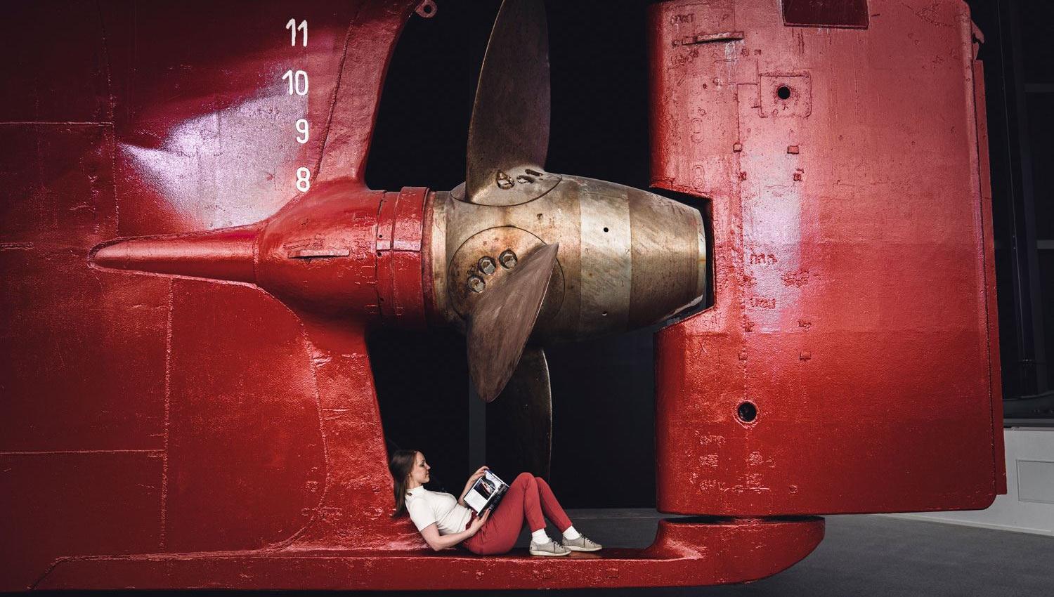 Jente sitter under propellen på MS Finnmarken og leser bok