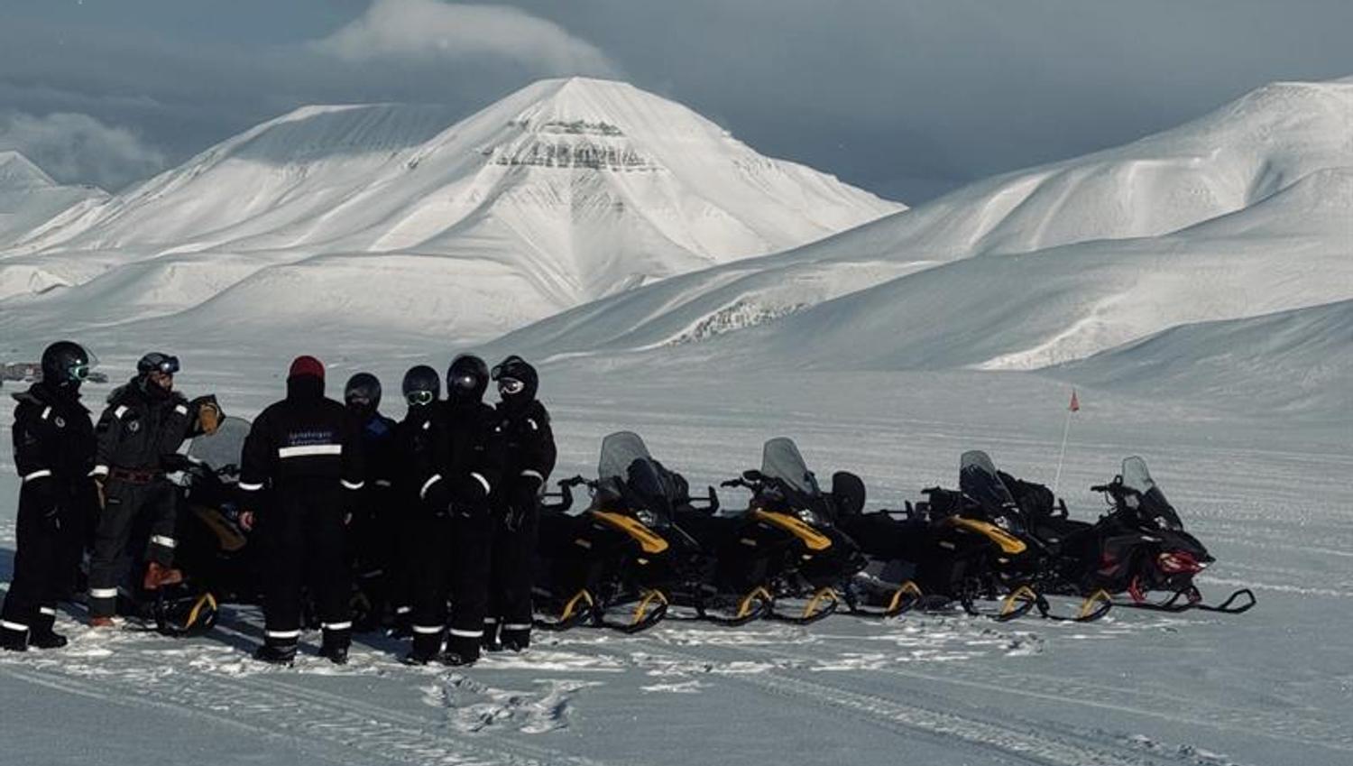 A group of people are standing in the winter landscape around snowmobiles
