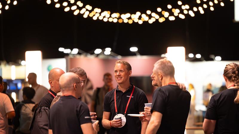 Flere personer med navneskilt står i en gruppe og snakker sammen under en konferanse eller nettverksarrangement.