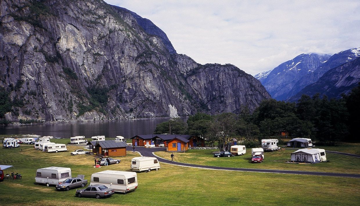 Utsikt over campingplassen med hytter, biler og campingvogner.