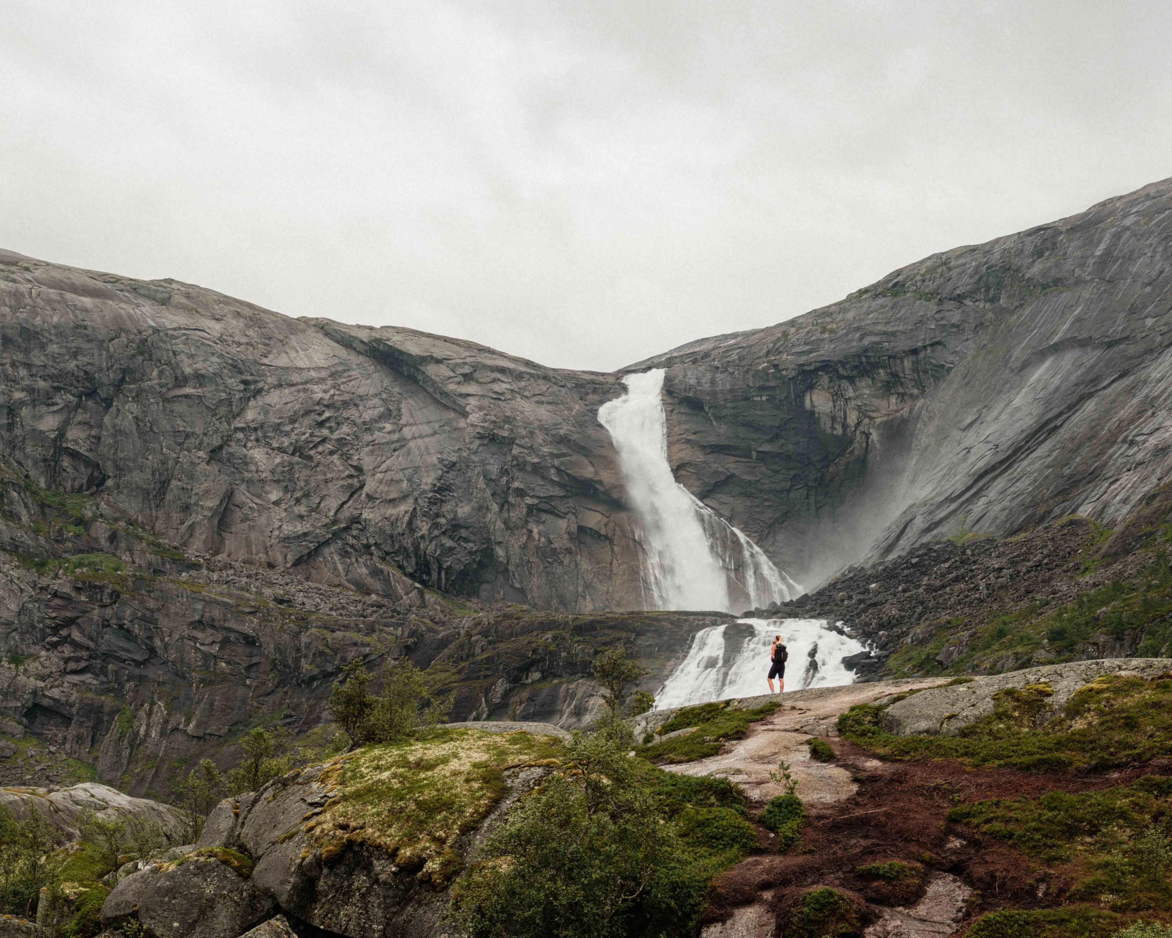 Zwei Wanderer stehen vor dem imposanten Wasserfall Søtefossen in Husedalen, umgeben von steilen Felsen und tosenden Wassermassen.
