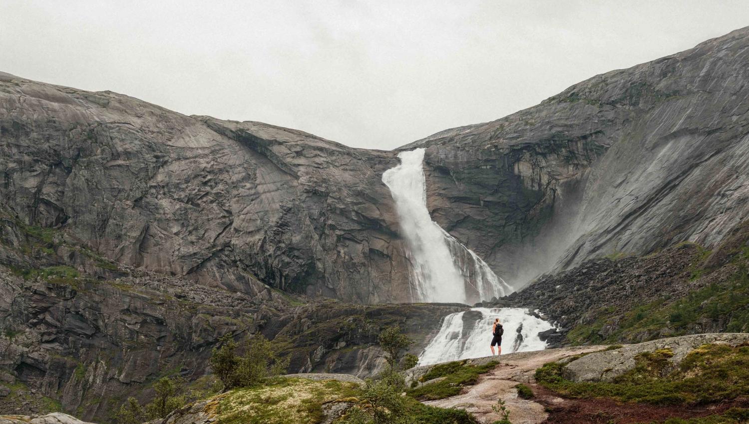 To turgåarar står framfor den mektige Søtefossen i Husedalen, omringa av dramatiske fjell og fossande vatn.