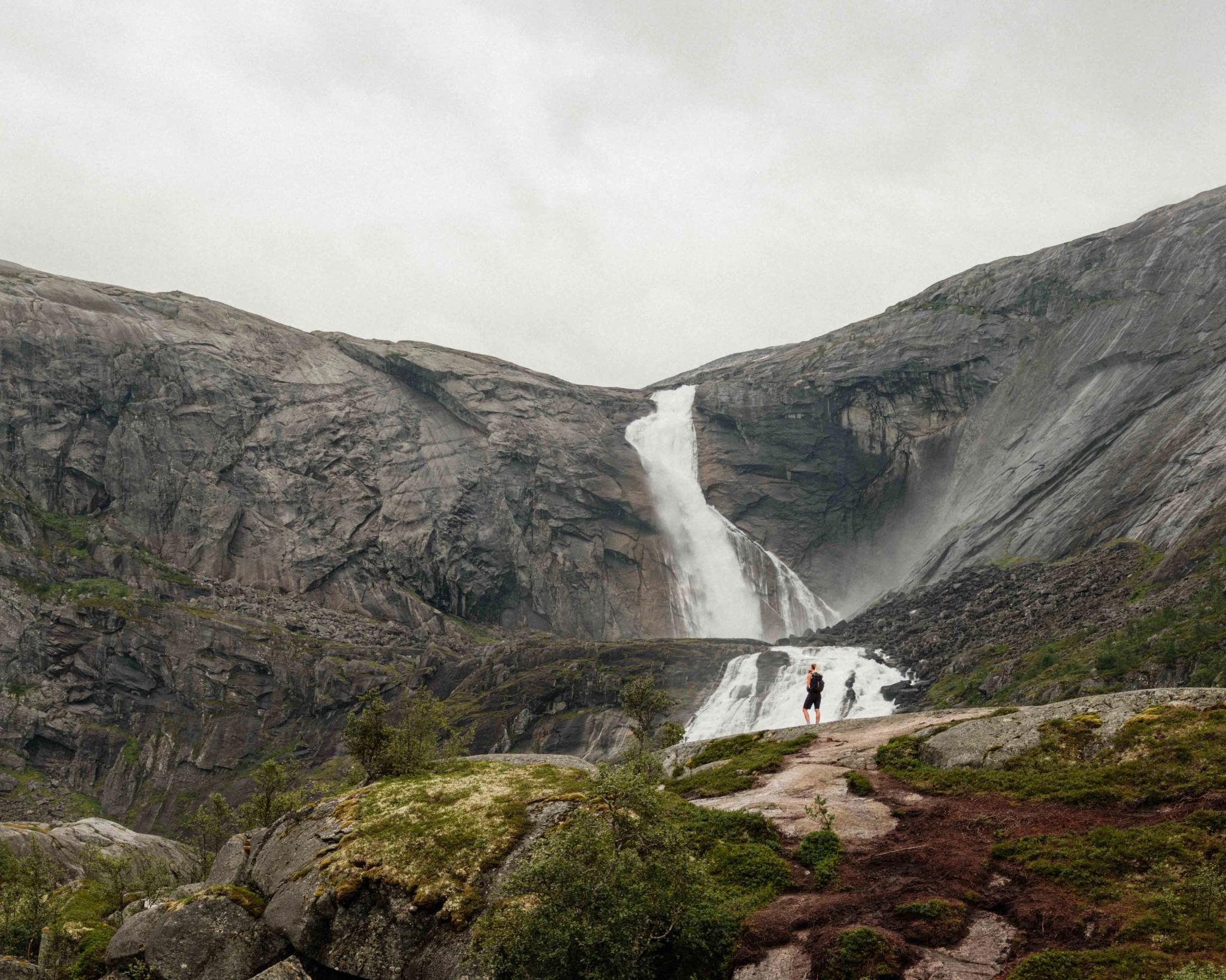 Zwei Wanderer stehen vor dem imposanten Wasserfall Søtefossen in Husedalen, umgeben von steilen Felsen und tosenden Wassermassen.