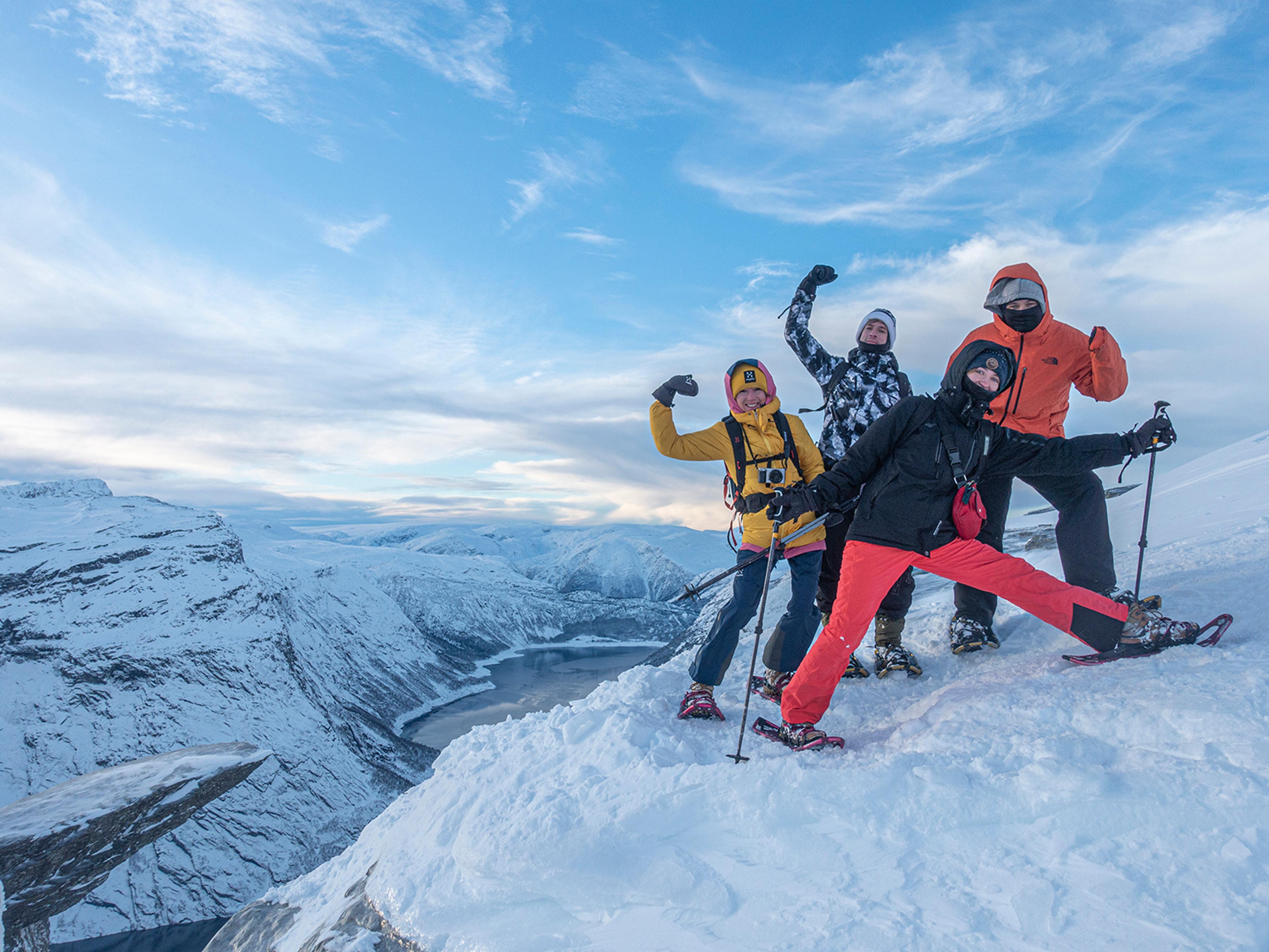 Gruppe vintervandrere poserer ved Trolltunga på snødekt fjellplatå med fjordutsikt.