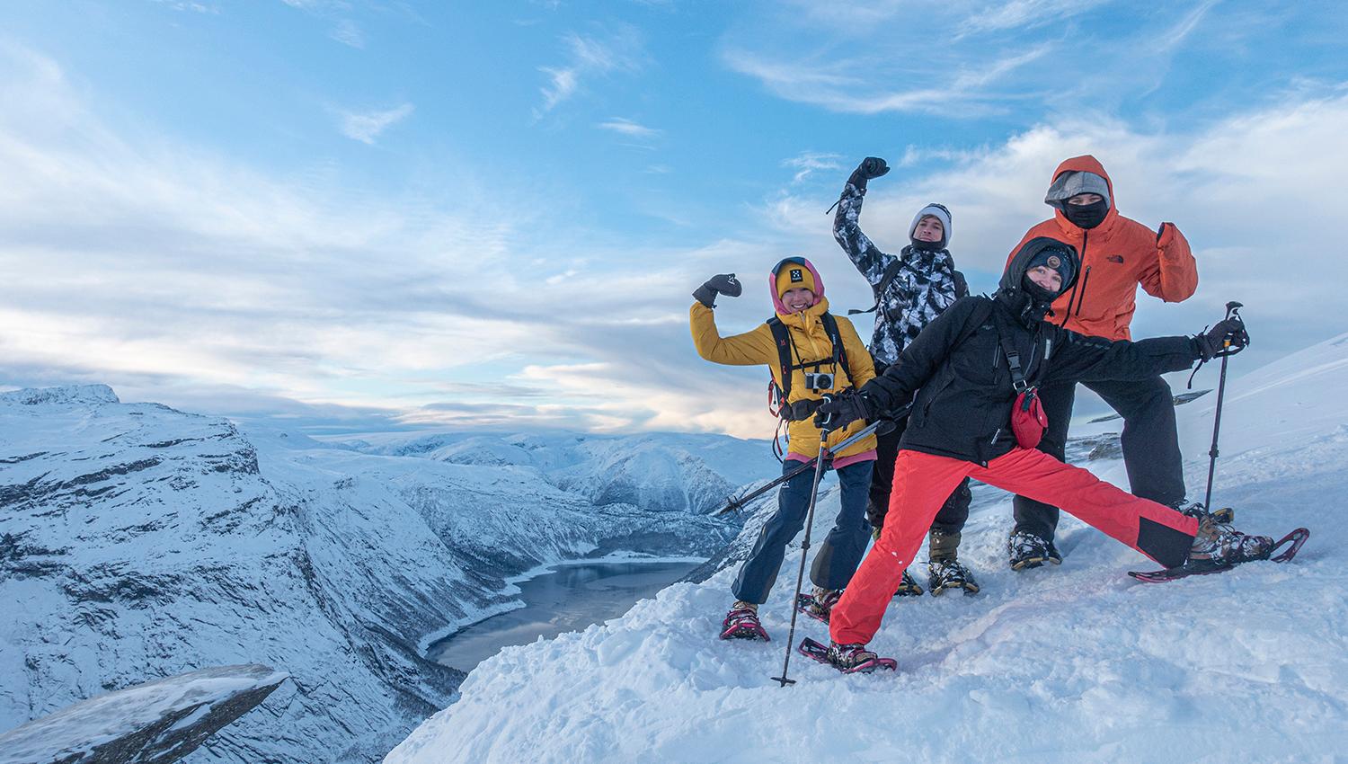 Group of winter hikers posing near Trolltunga on a snowy mountain plateau with fjord views.