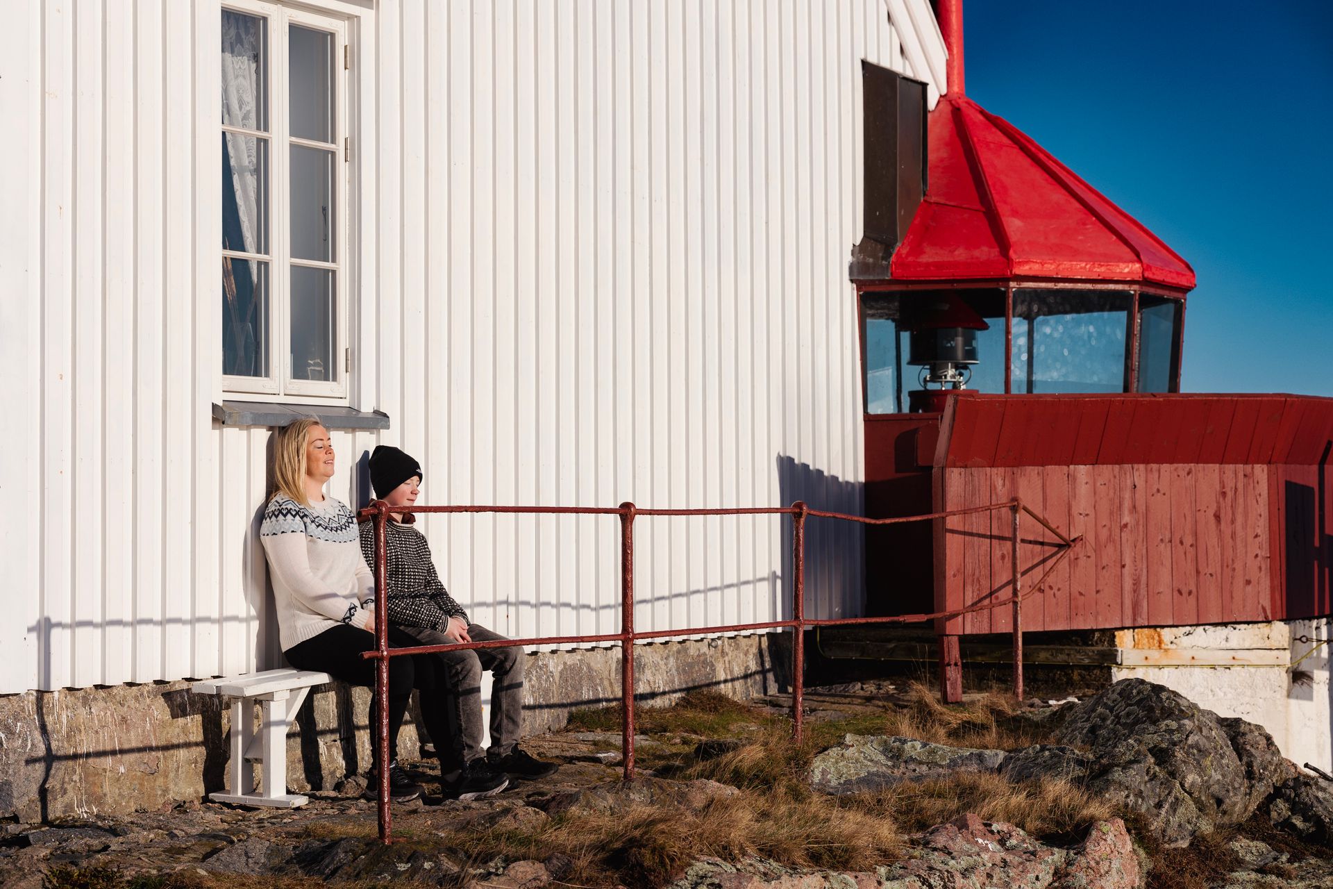 To personer som sitter i solveggen ved Hatholmen fyr