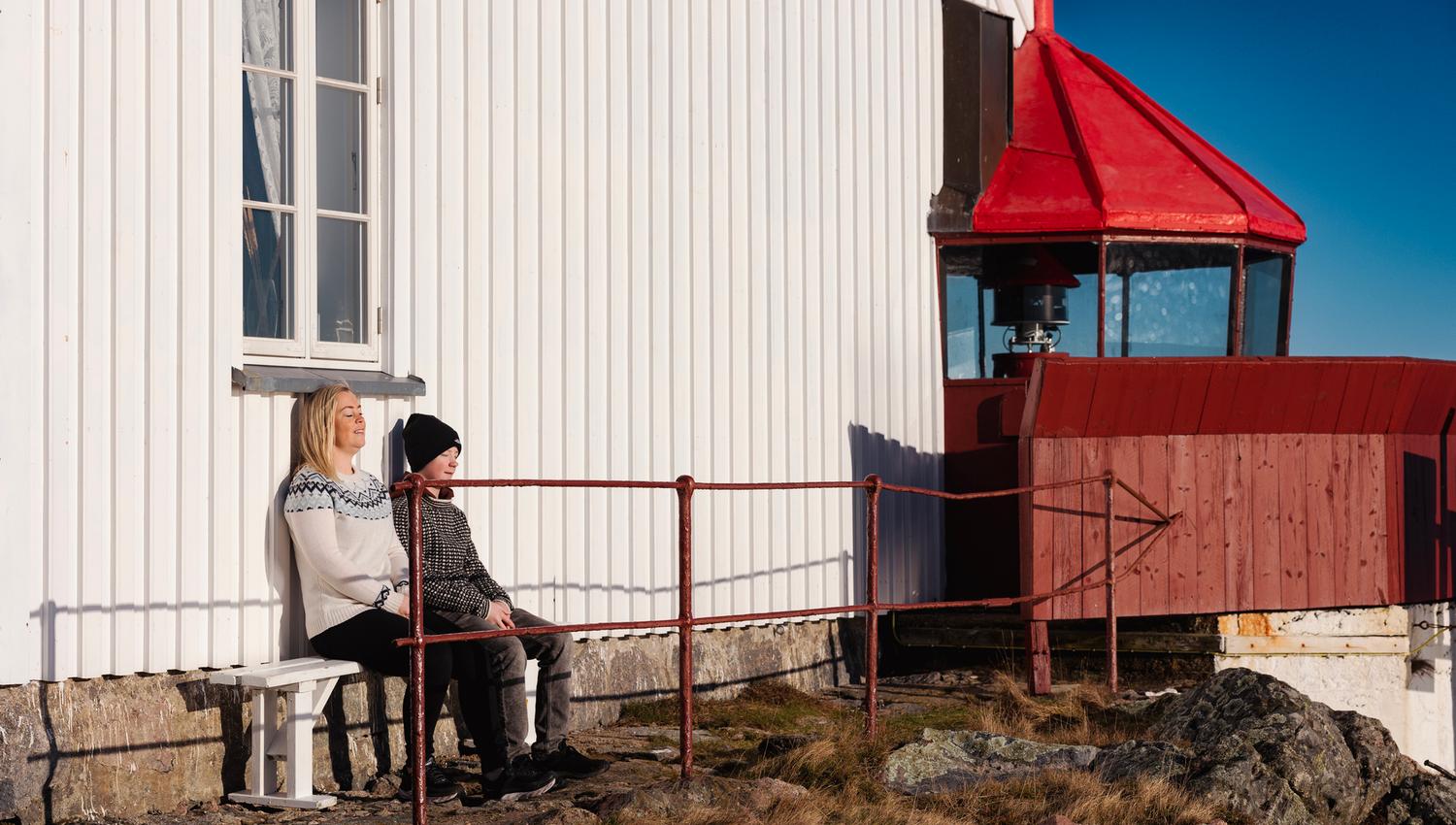 To personer som sitter i solveggen ved Hatholmen fyr