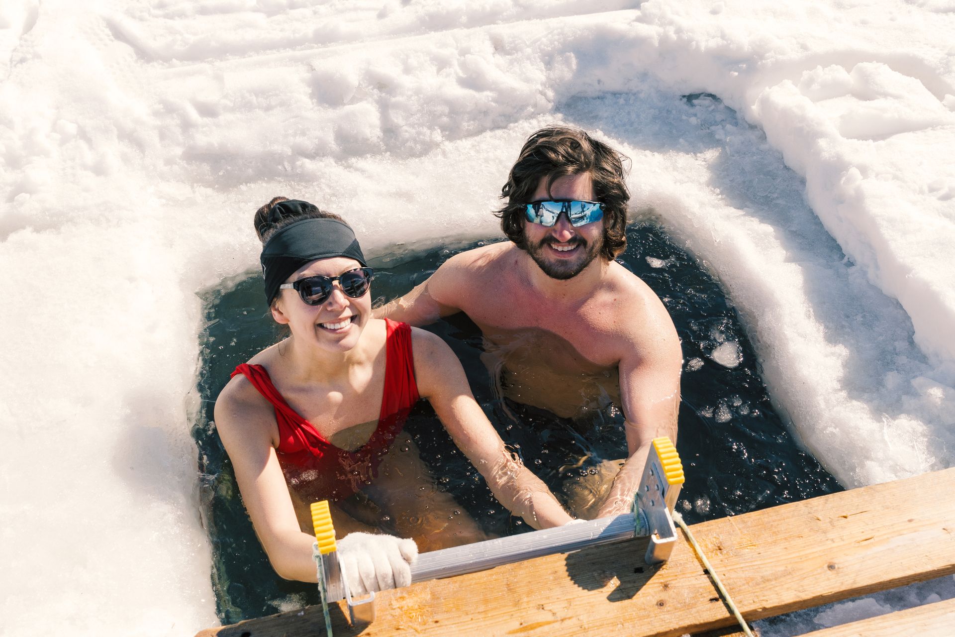 A couple  enjoying an ice bath with a snow-covered landscape behind them. 