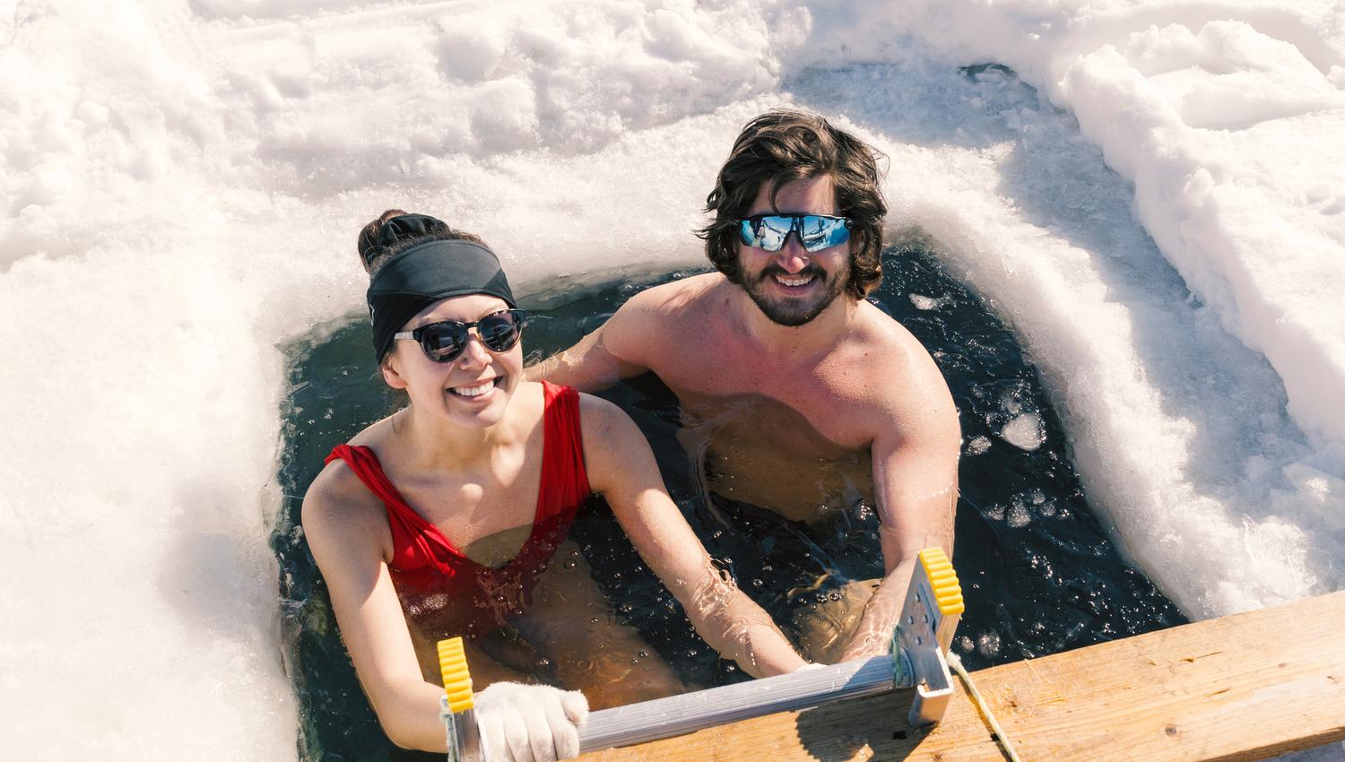 A couple enjoying an ice bath with a snow-covered landscape behind them.
