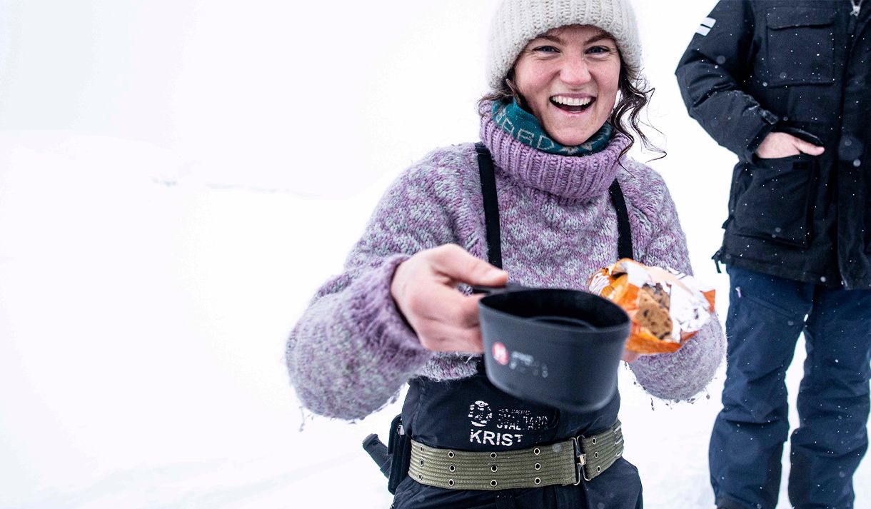 A guide offering something hot to drink in a cup and cookies during a break on a trip