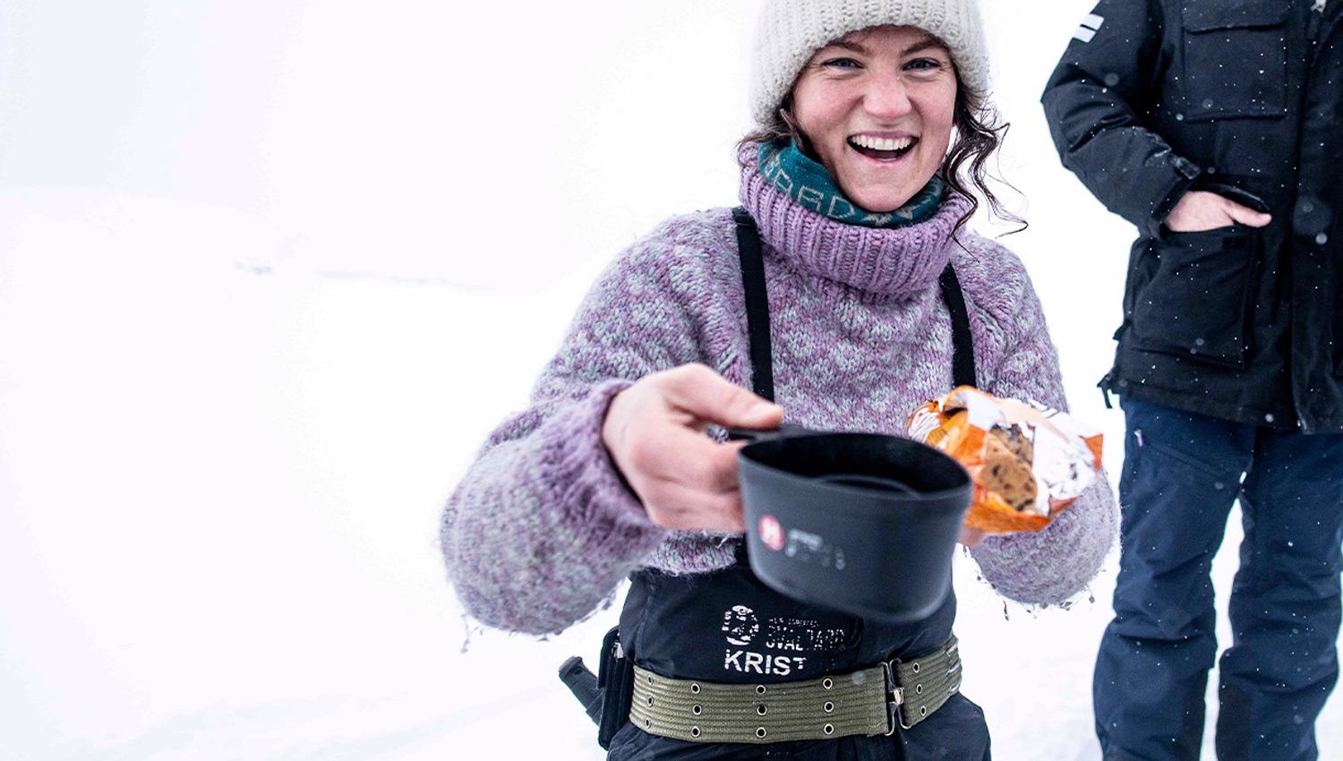 A guide offering something hot to drink in a cup and cookies during a break on a trip