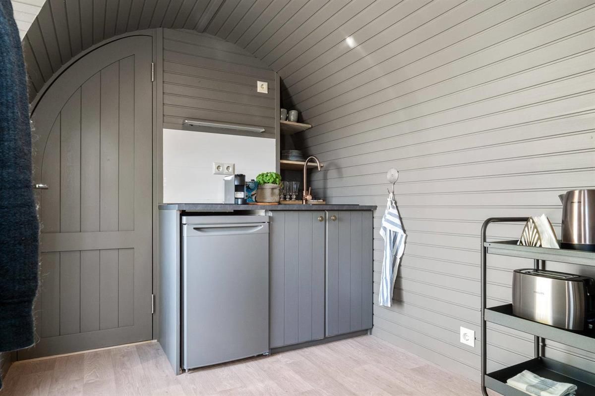  Small kitchenette with a fridge and storage inside a wooden cabin pod.