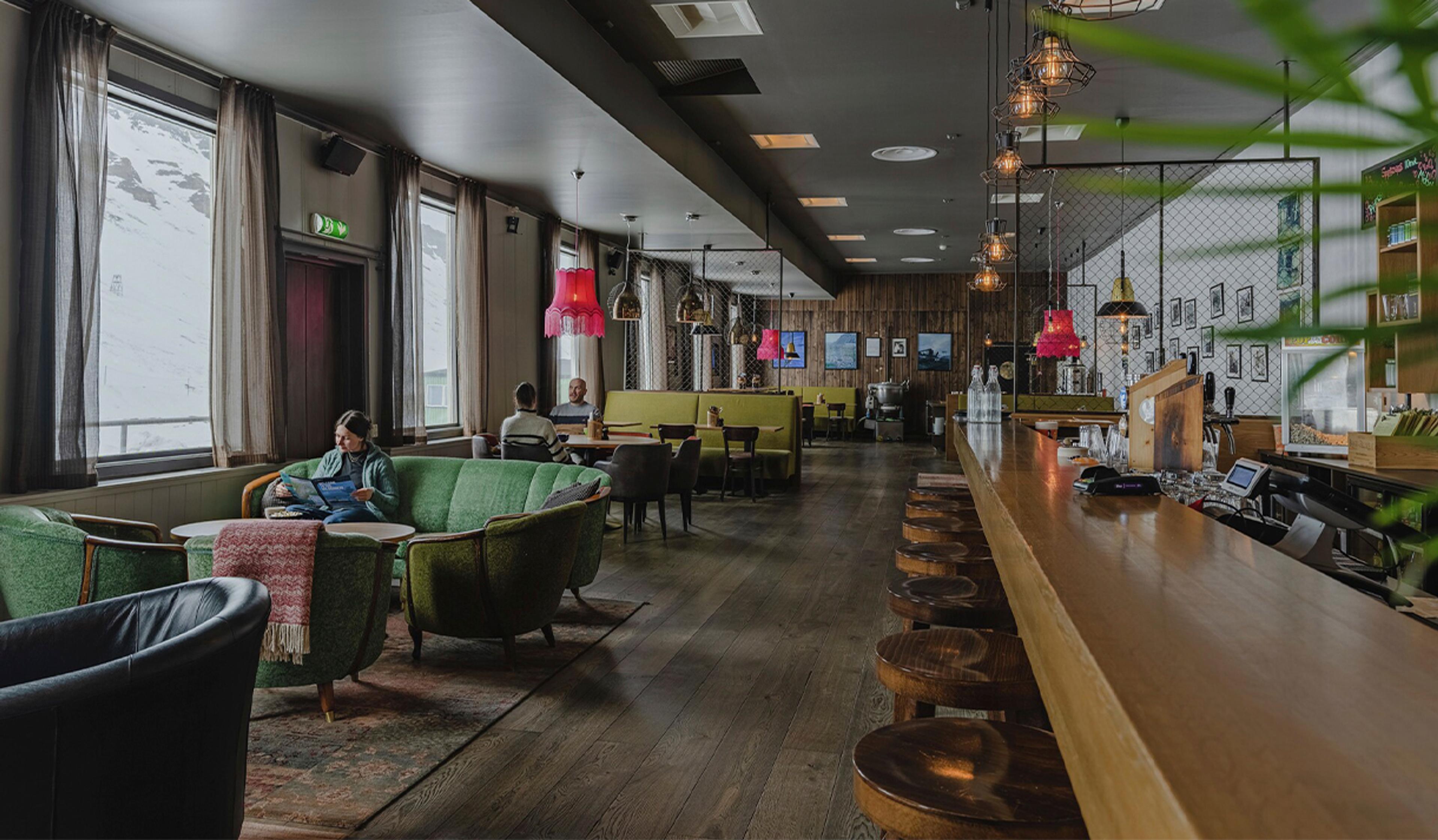 A reception desk and lounge with a guest seated in a couch in the foreground, with restaurant tables and two guests seated at a table in the backgroun