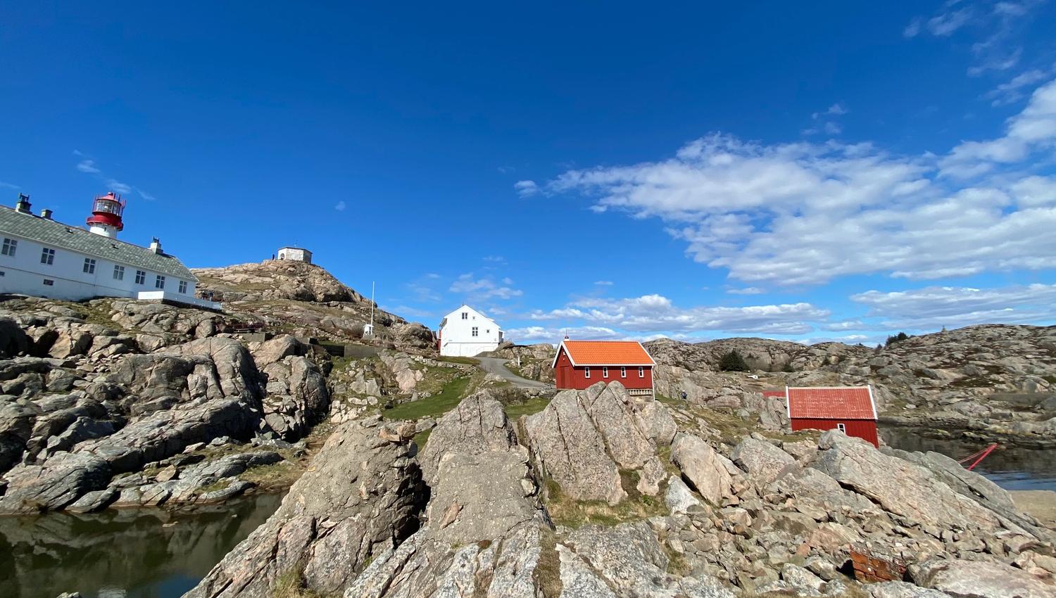 Utsikt fra homen opp mot fyrtårnet og andre bygninger i rødt og hvitt