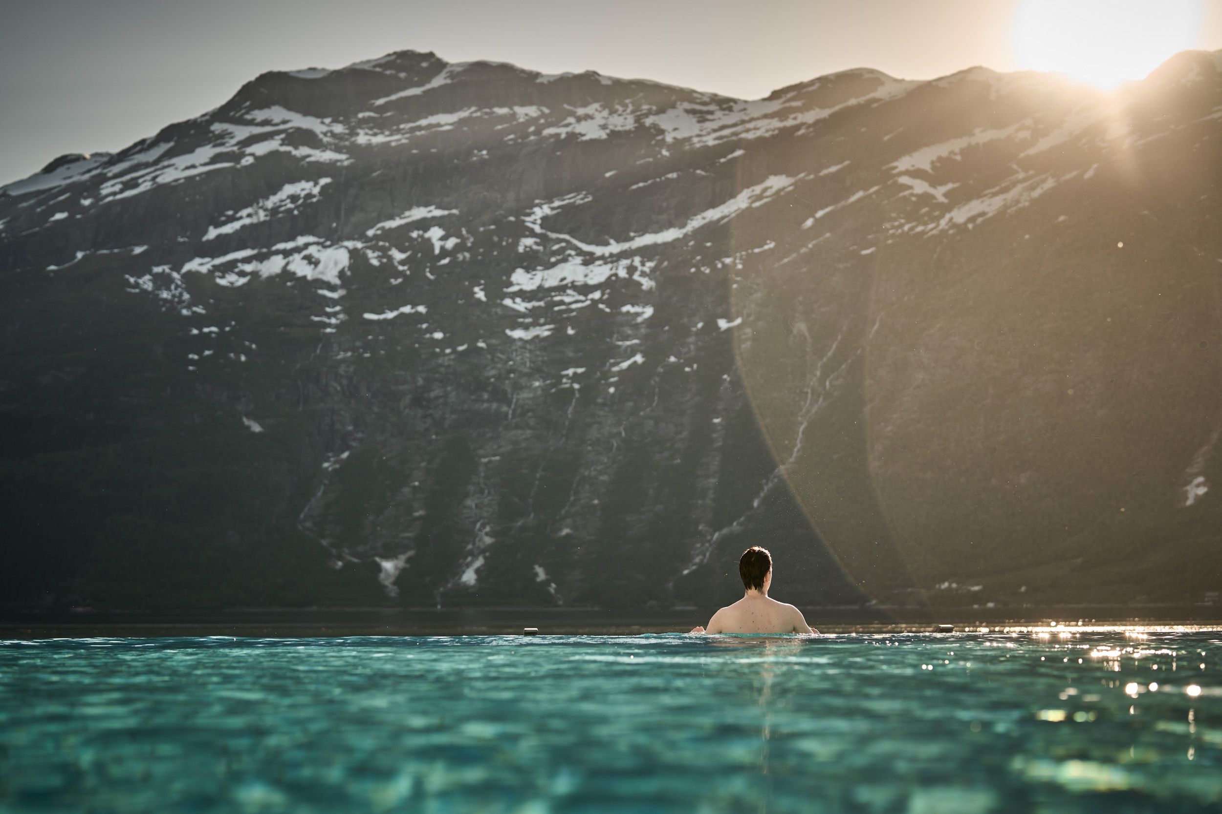 Ein gjest nyt rolege kveldstimar i infinitybassenget med solnedgang over fjella.