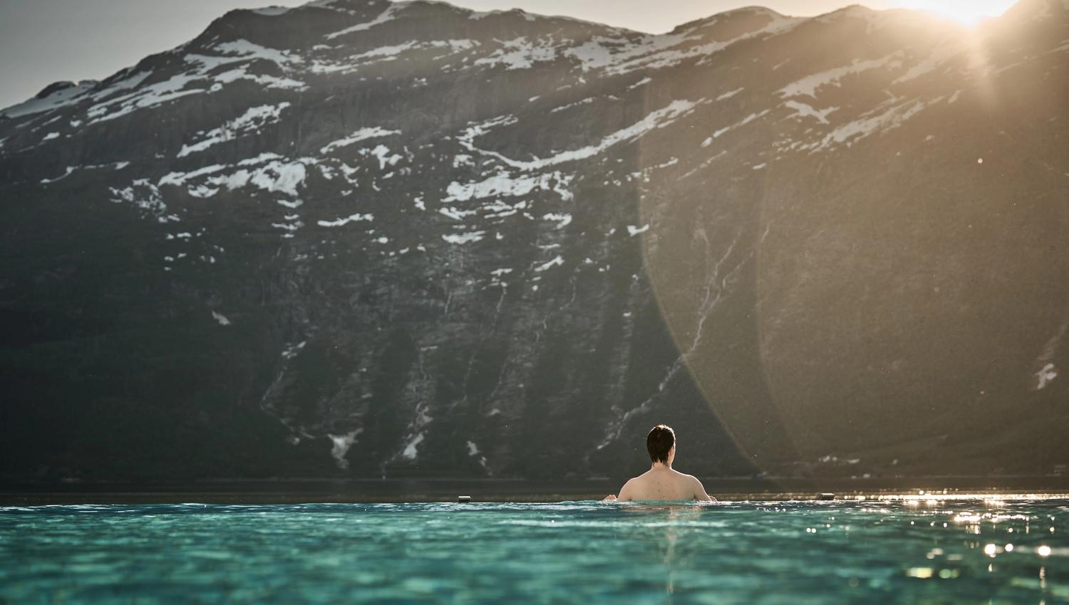 Ein gjest nyt rolege kveldstimar i infinitybassenget med solnedgang over fjella.