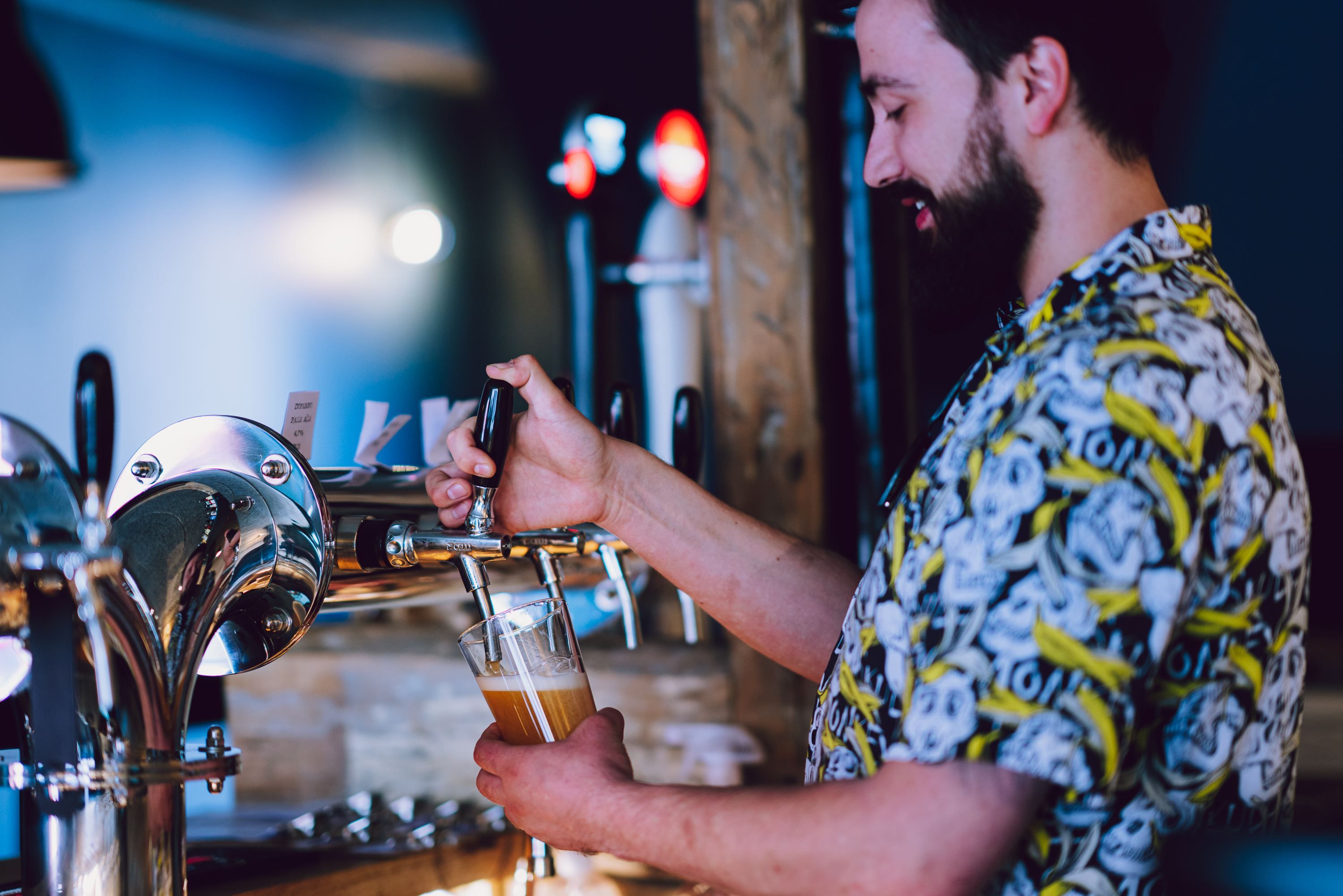 Person pouring beer from a tap in a bar with several beer taps in the background.