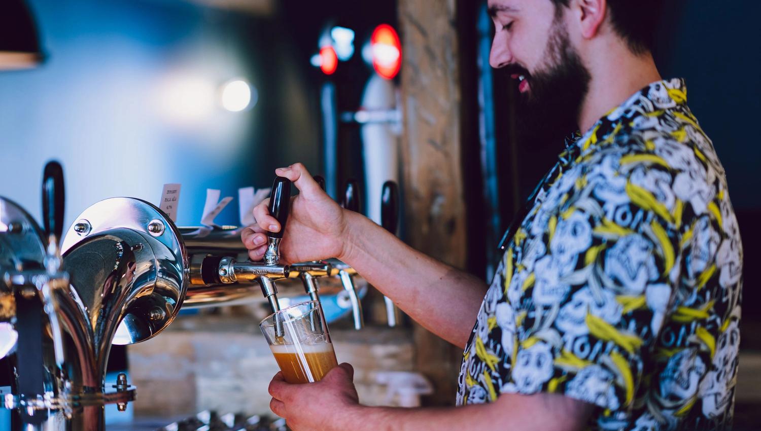 Person pouring beer from a tap in a bar with several beer taps in the background.