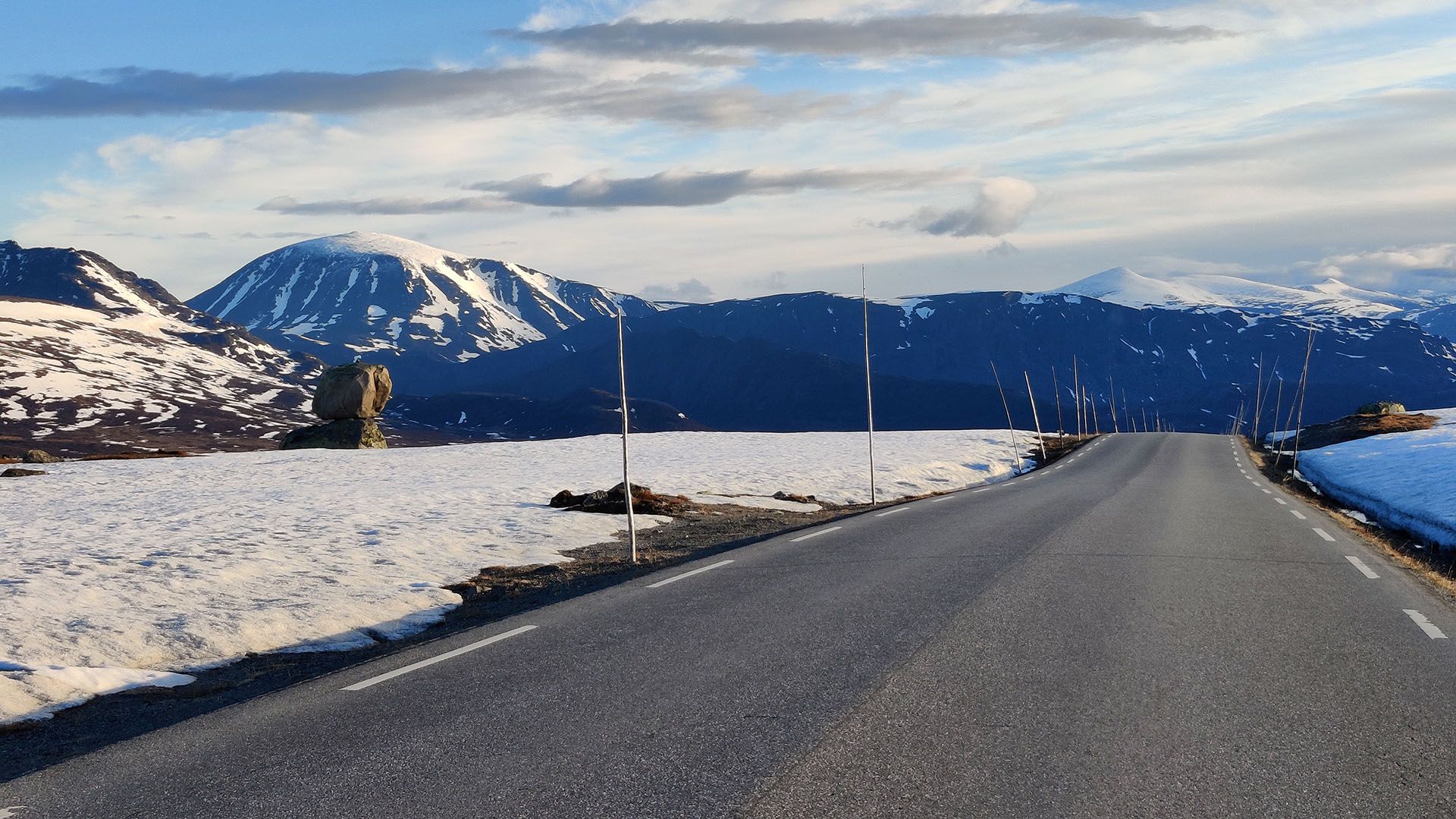 Vei over snødekt fjellplatå med snødekte fjell i bakgrunnen.