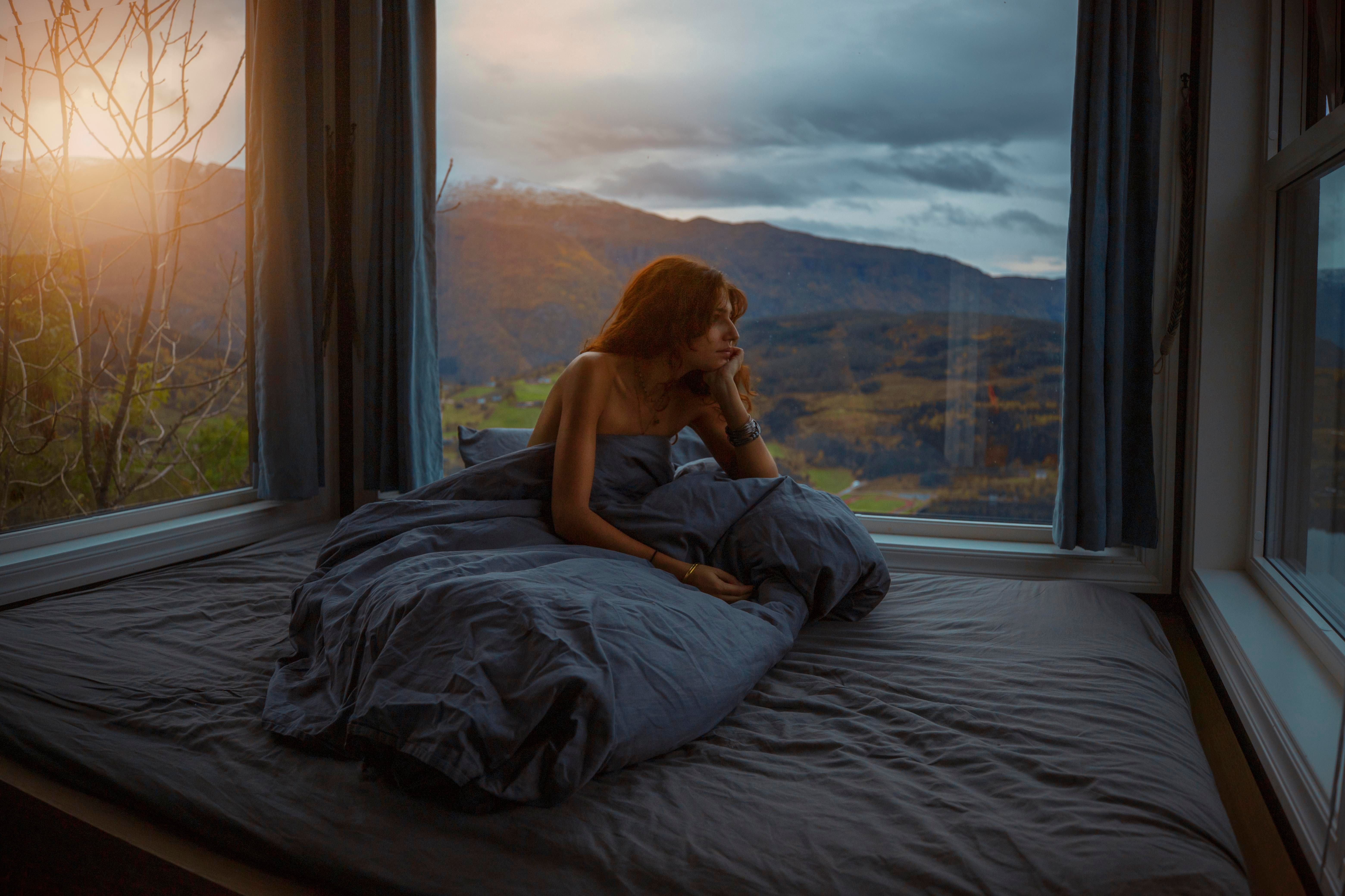 Kvinne slappar av med fjordutsikt frå soverommet i Hardanger Panorama Lodge.