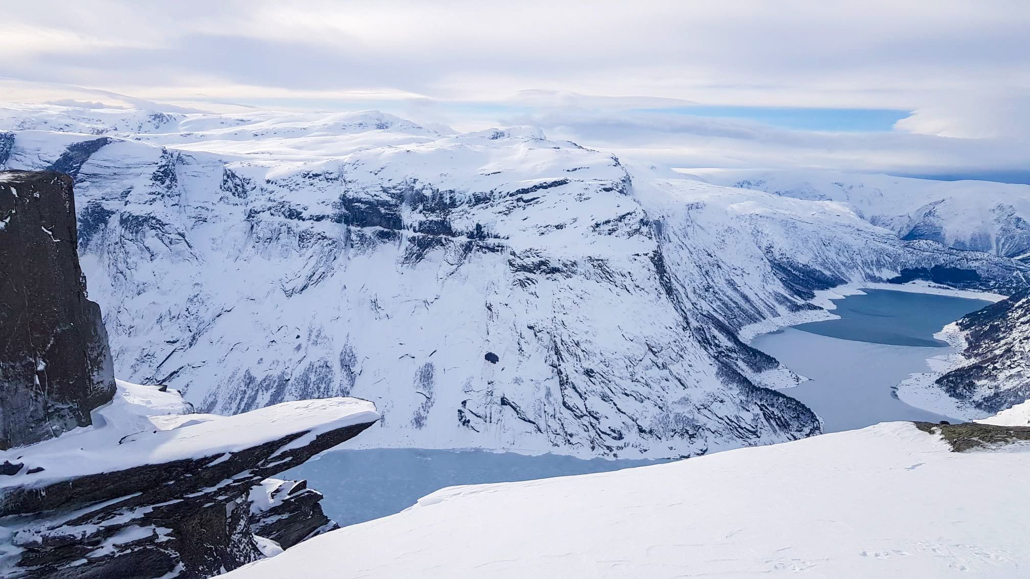 Trolltunga vinterlandskap med snødekte fjell og frossen fjord.