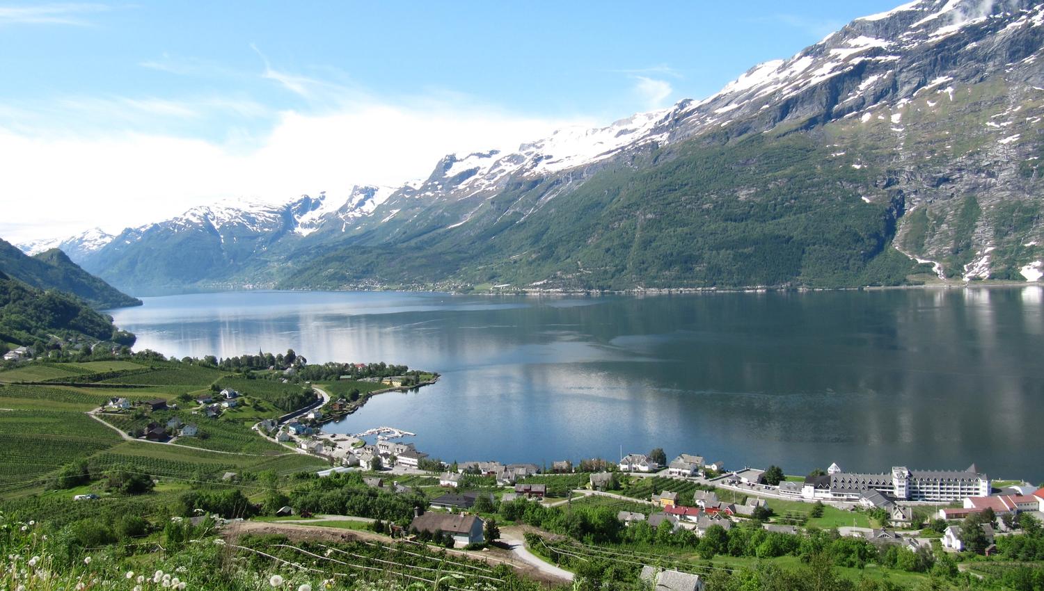 Utsikt over Sørfjorden og fruktbygdene i Hardanger, med snødekte fjell og glitrande vatn.