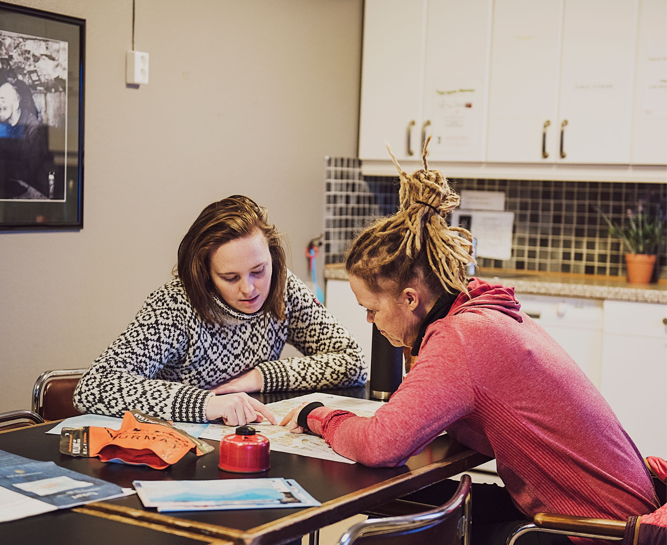 Two guests sitting at a table in a shared kitchen area at Coal Miners' Cabins planning a trip, with various outdoors equipment laid out on the table