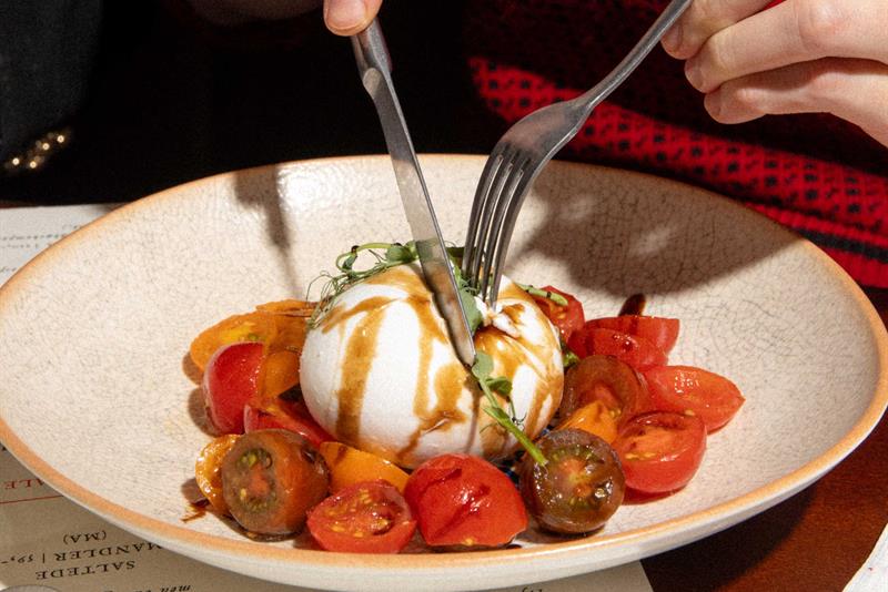 A guest cuts into a burrata served with tomatoes and dressing in a restaurant