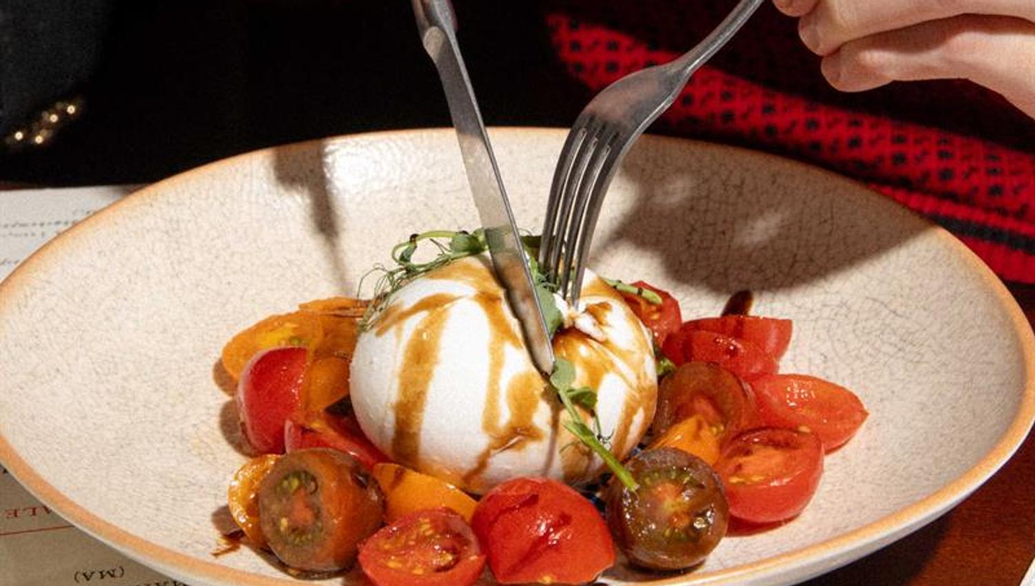 A guest cuts into a burrata served with tomatoes and dressing in a restaurant
