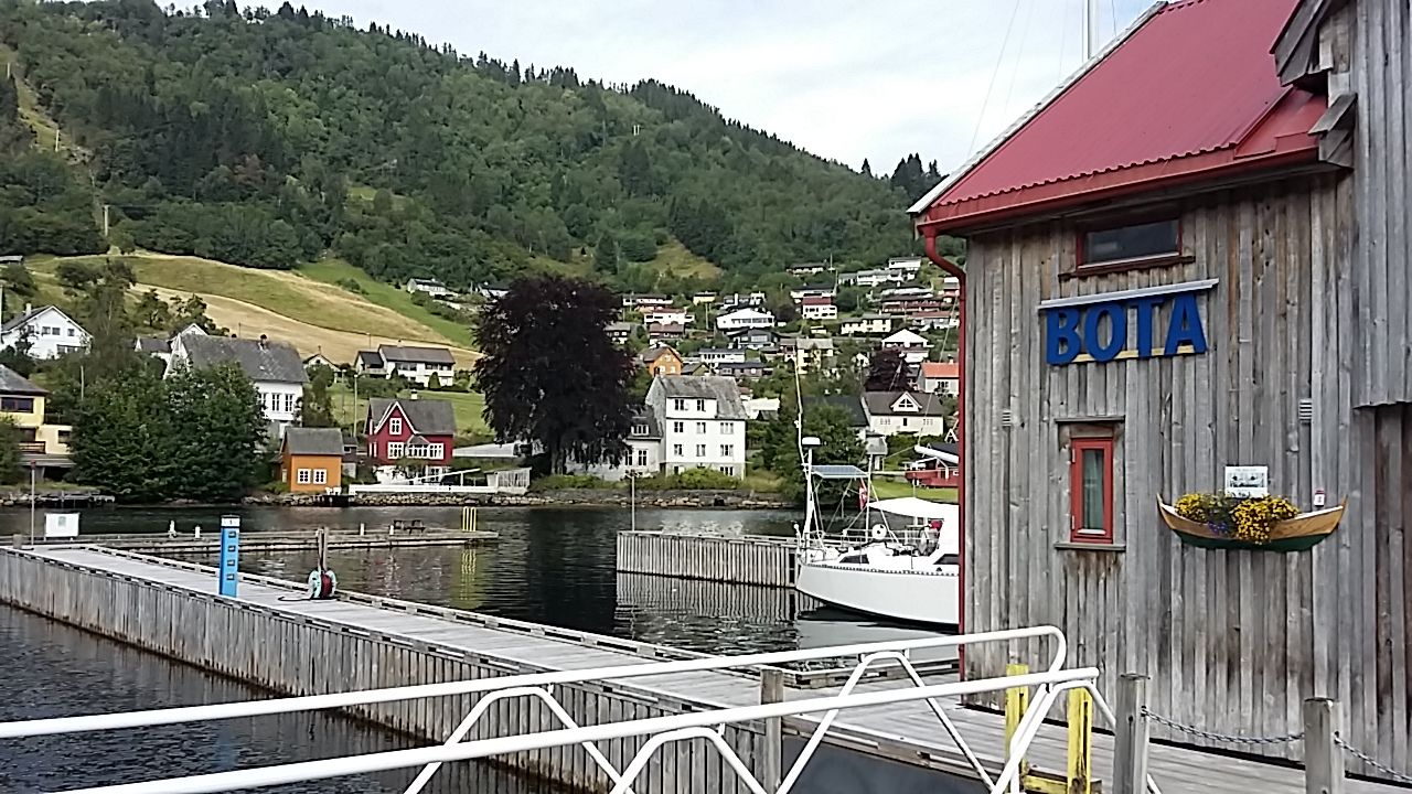 Trehus med raude tak og brygger ved Norheimsund Gjestehamn, med båtar og fjordutsikt.