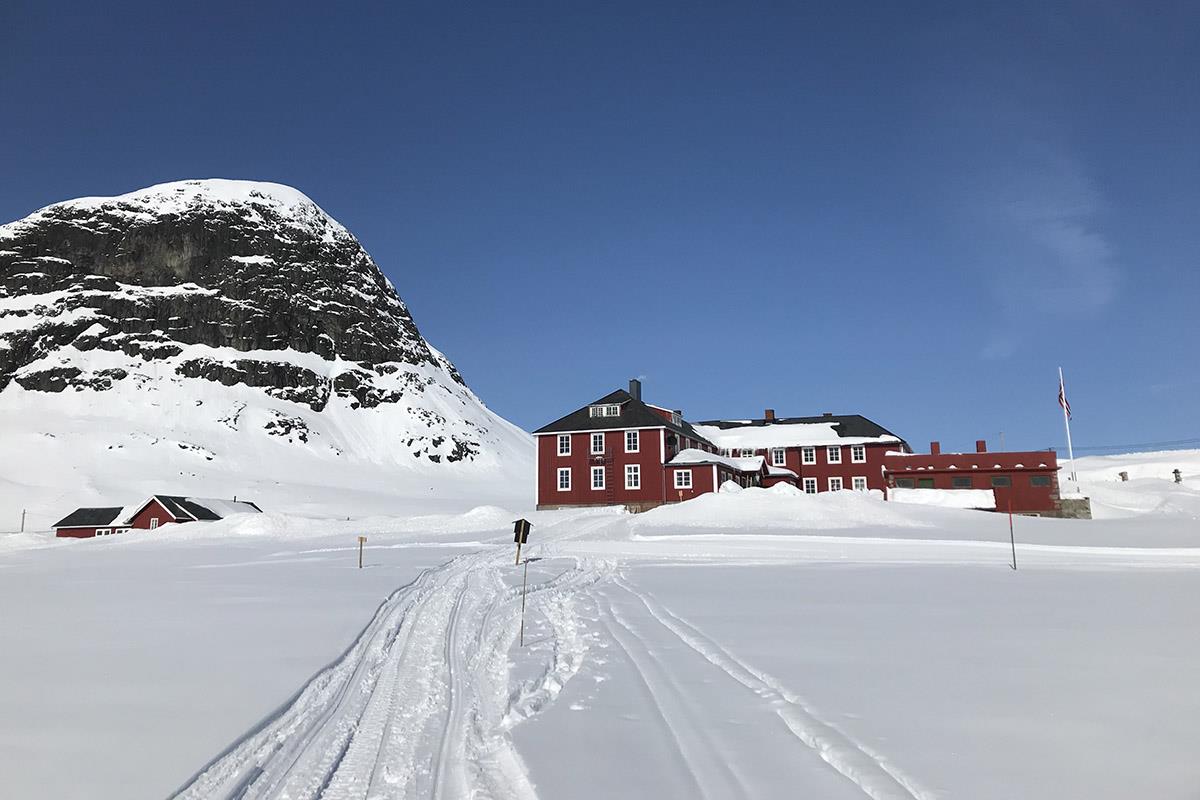 Rødt fjellhotell i vinterlandskap med løyper i for- og fjell i bakgrunnen
