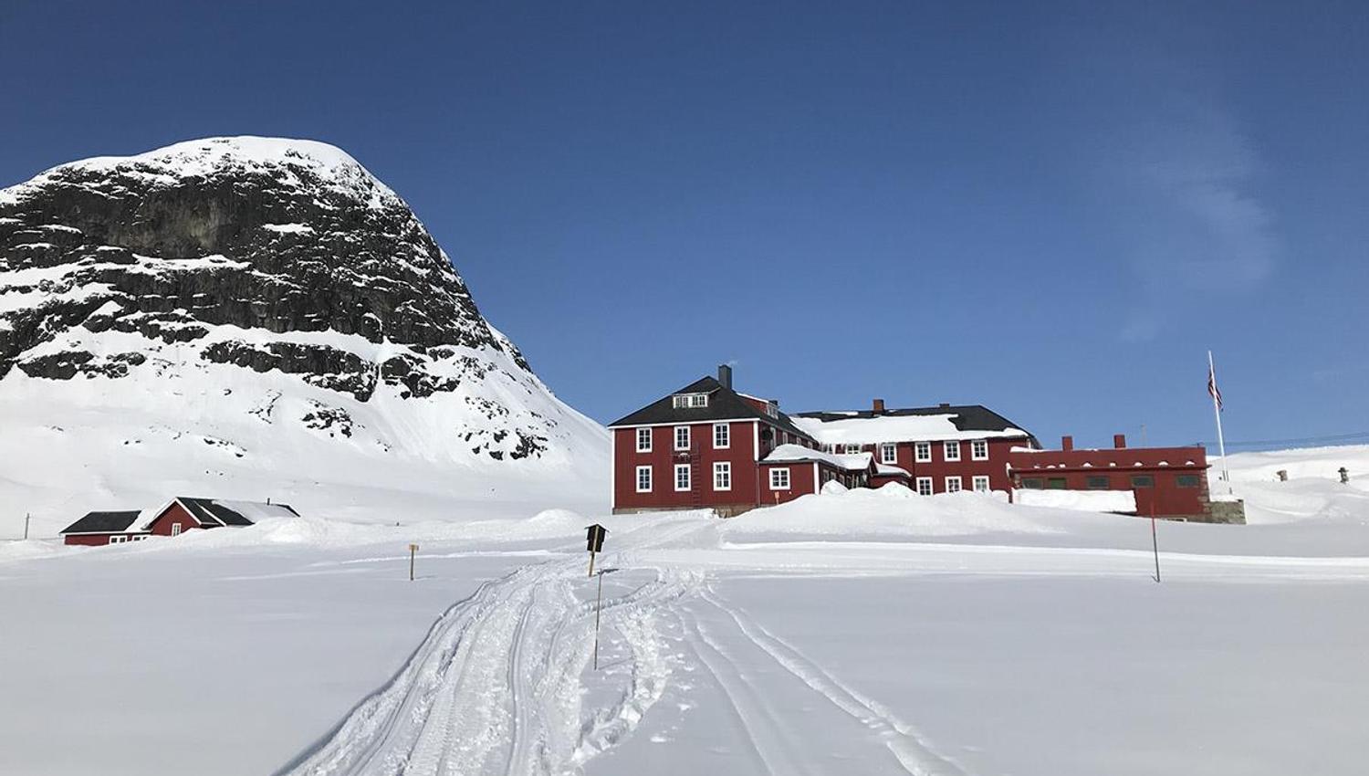 Rødt fjellhotell i vinterlandskap med løyper i for- og fjell i bakgrunnen