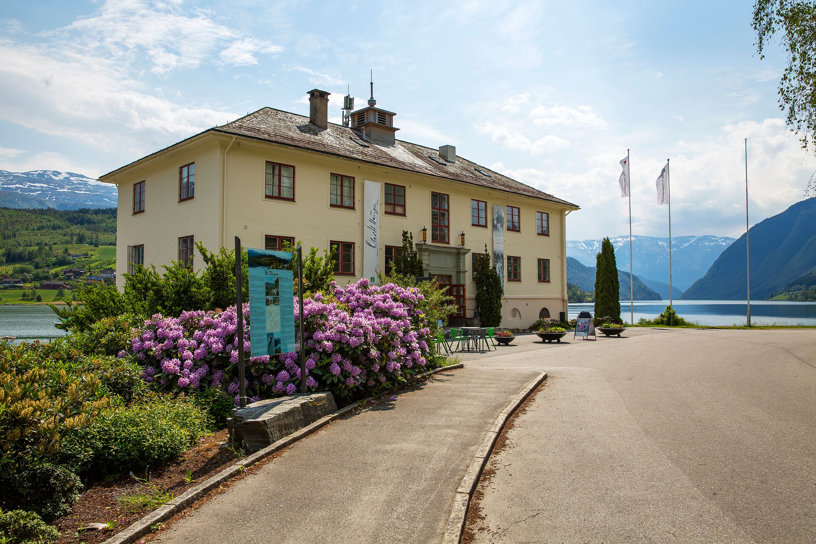 Haugesenteret ligg vakkert til ved fjorden i Hardanger, med fjell og blømande rododendron i bakgrunnen.