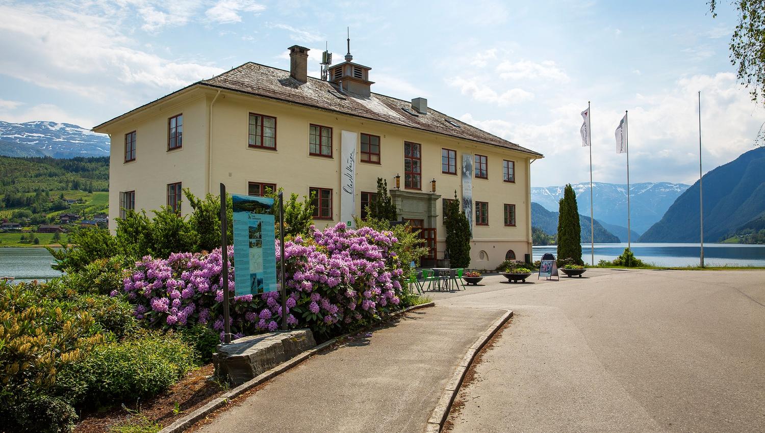 Haugesenteret ligg vakkert til ved fjorden i Hardanger, med fjell og blømande rododendron i bakgrunnen.