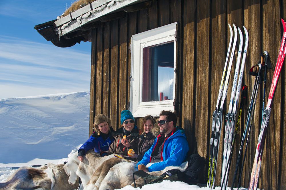 2 par som sitter foran hytten på vinter og nyter solen