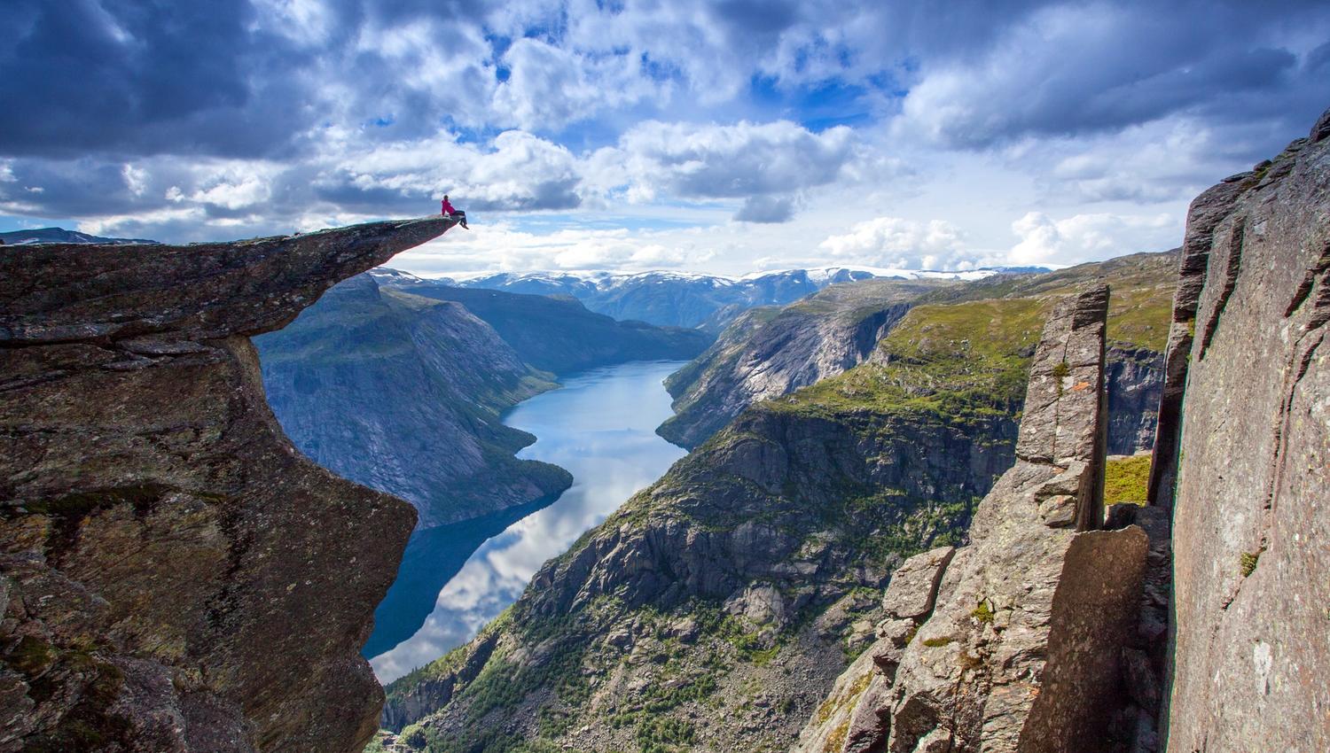Person sitting on Trolltunga cliff with dramatic fjord and mountain landscape in Hardangervidda, Hardanger.