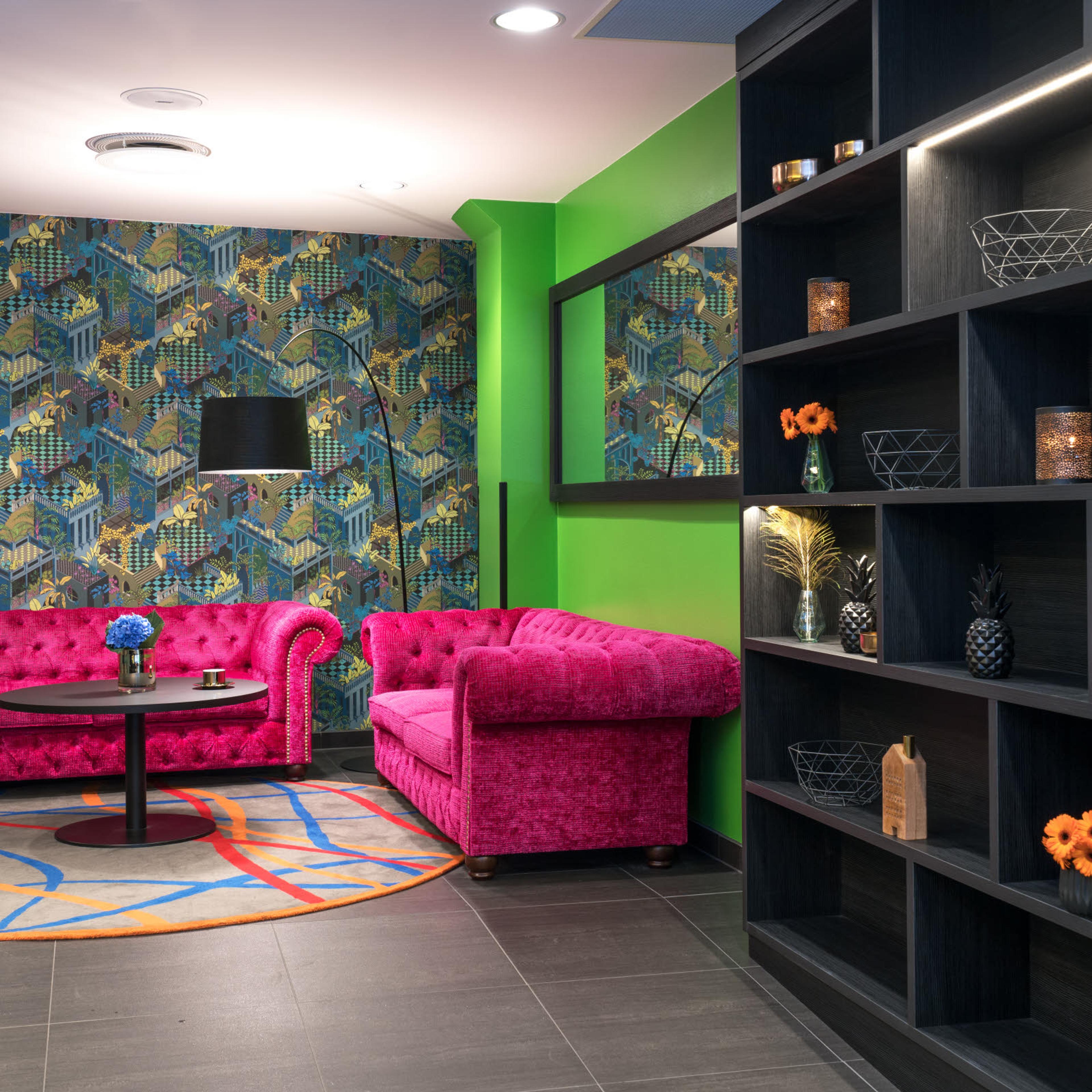 To sofaer i pink foran en eplegrønn vegg og en tapetvegg. Thon Hotel Terminus i Oslo. Foto.