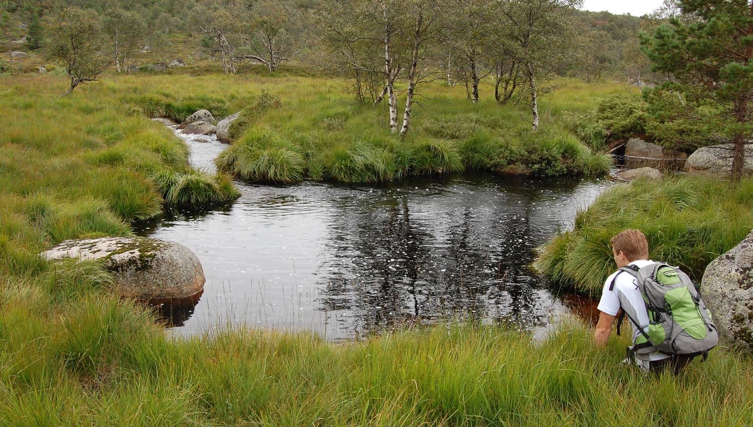 En slette med en mann som sitter på huk og ser ned på vannet