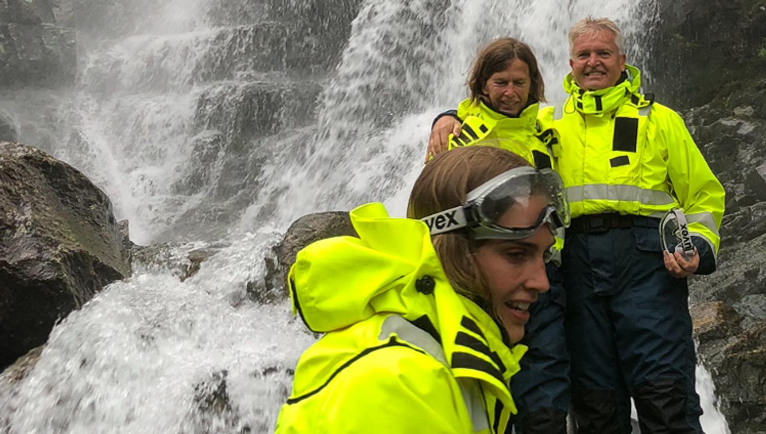 Spente deltakarar står tett inntil fossen og kjenner den kraftige vasspruten på RIB-safari i Hardanger.