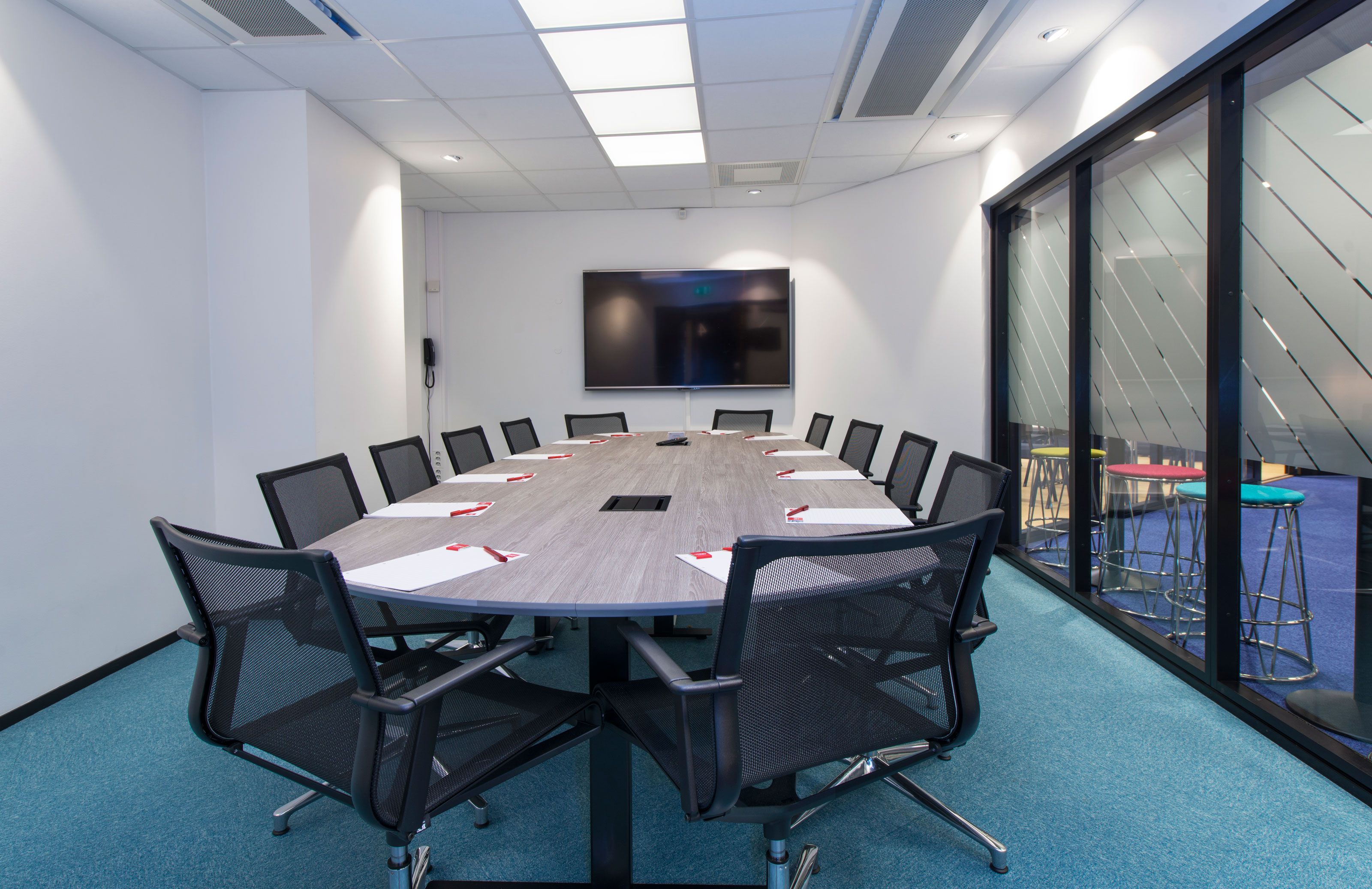 konferanserom med stort konferansebord, kontorstoler og TV-skjerm
