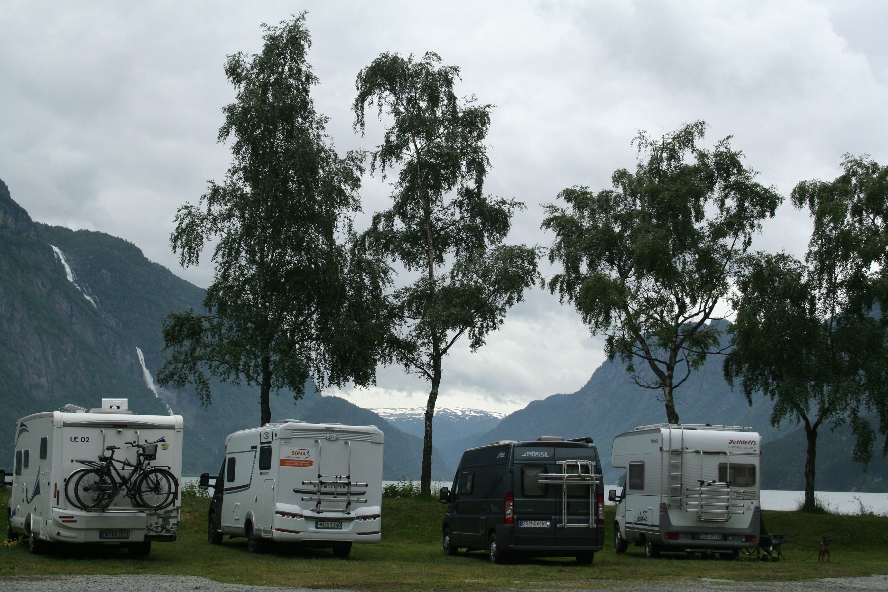 Bubilar parkert ved fjorden med foss og fjell bak.