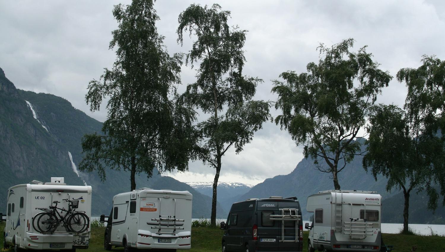 Bubilar parkert ved fjorden med foss og fjell bak.
