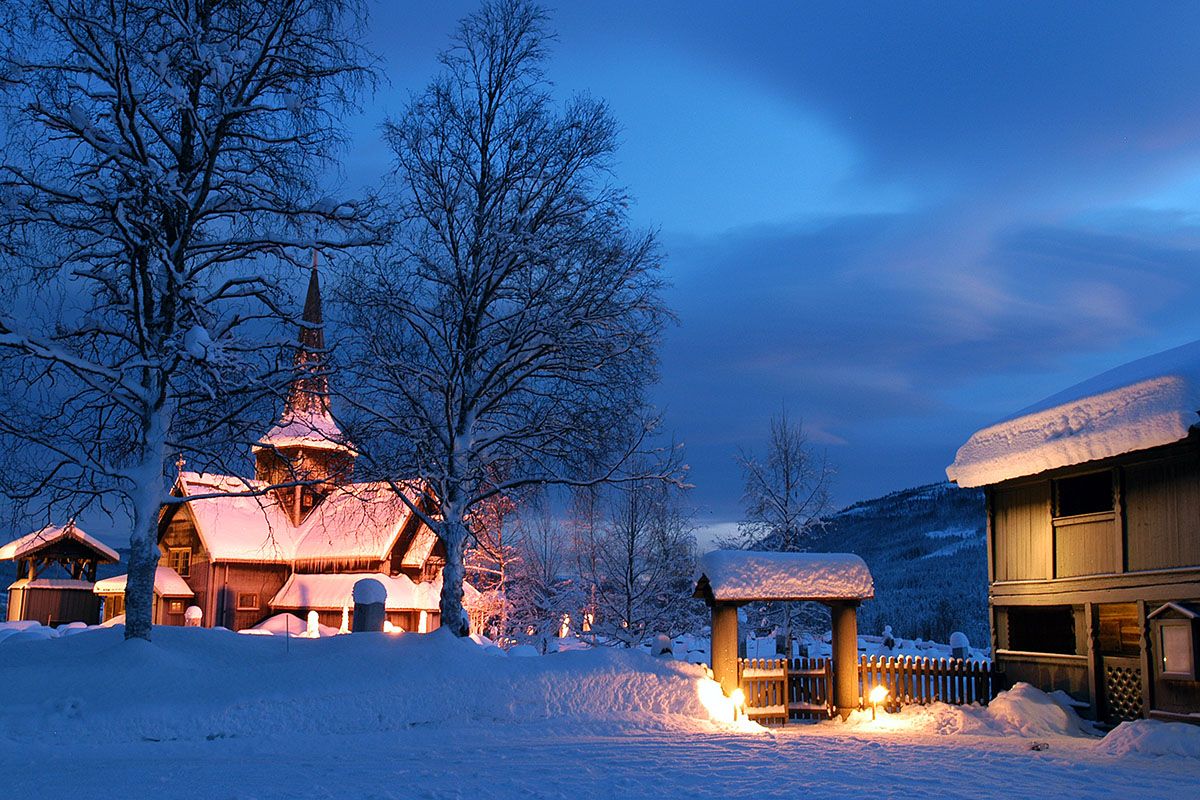 Hedalen stavkirke i blåtimen med fakler utenfor.