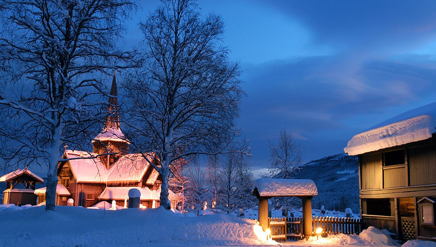 Hedalen stavkirke i blåtimen med fakler utenfor.