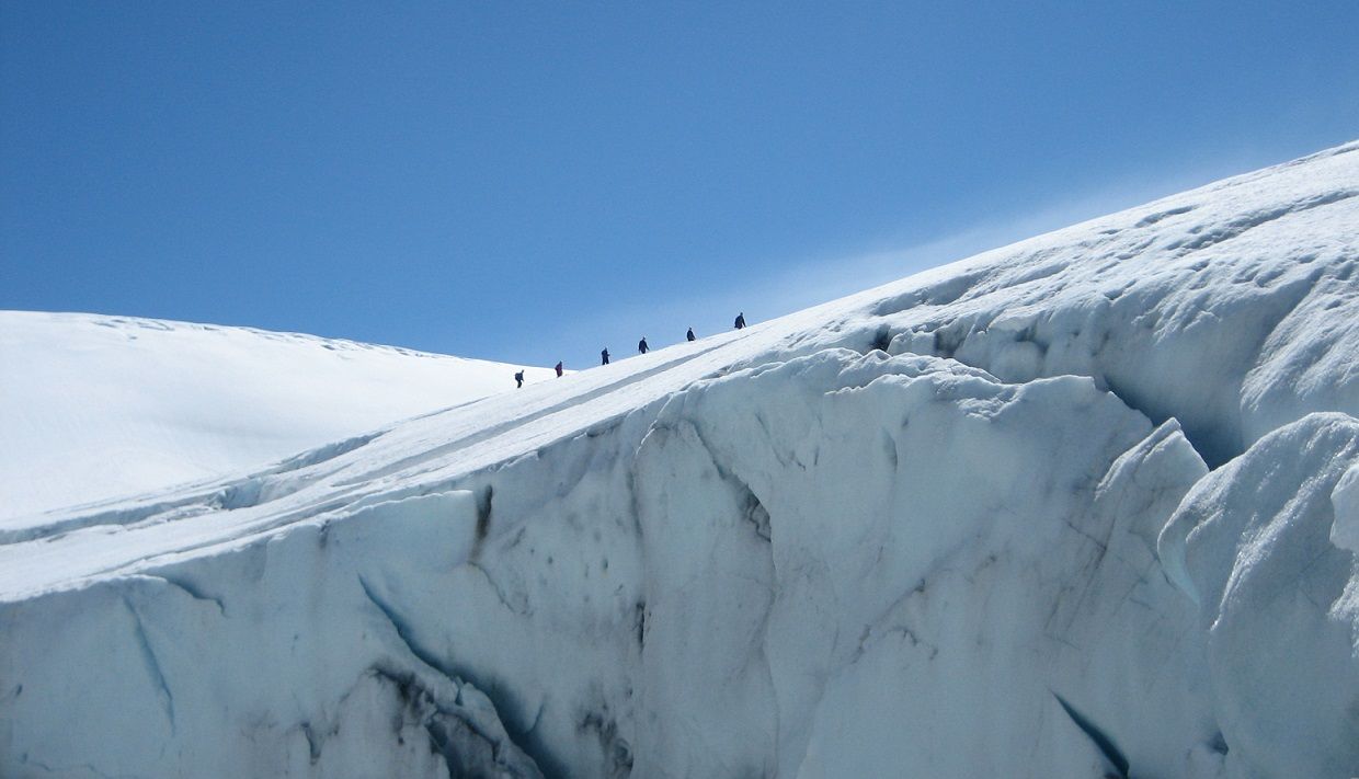 Små turgåargrupper beveger seg langs toppen av Folgefonna-breen med majestetiske isbre-sprekkar under seg.