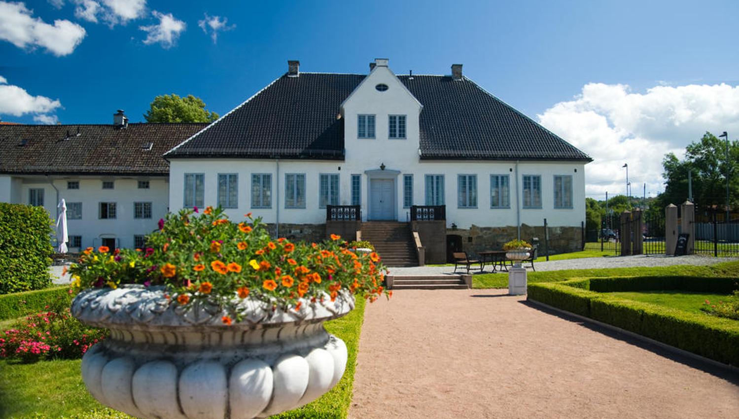 Eksteriør: Hvit lystgård fra barokkepoken med gressplen foran.
