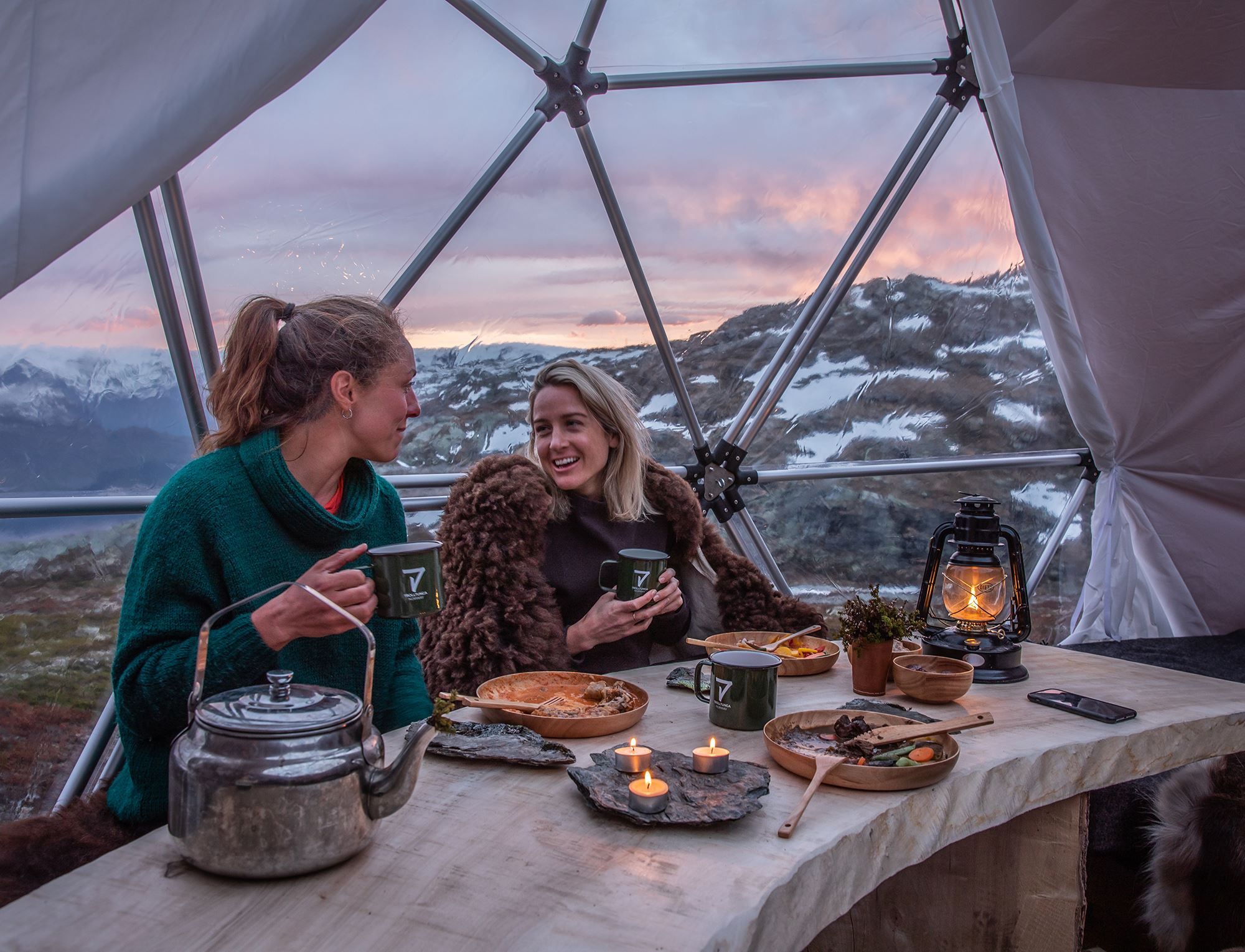 Two guests enjoying warm food and candlelight inside the glamping dome near Trolltunga.