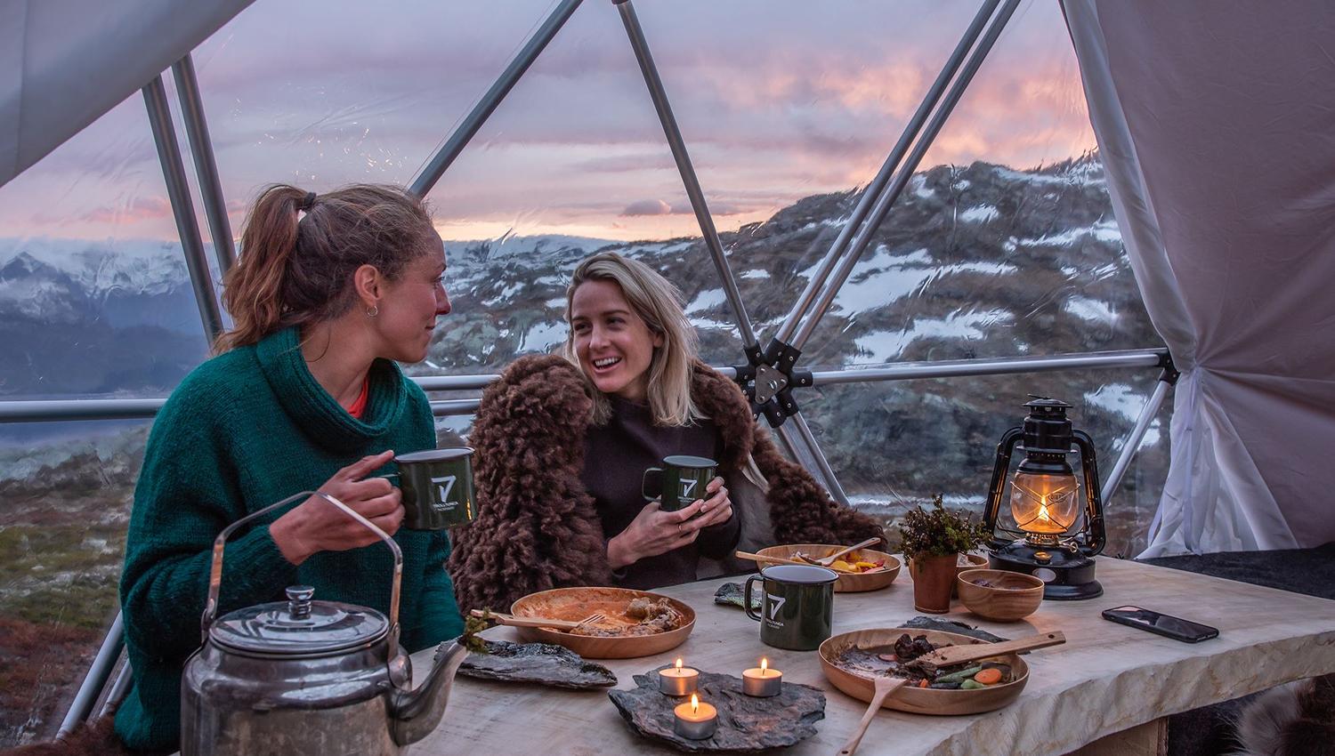 Two guests enjoying warm food and candlelight inside the glamping dome near Trolltunga.