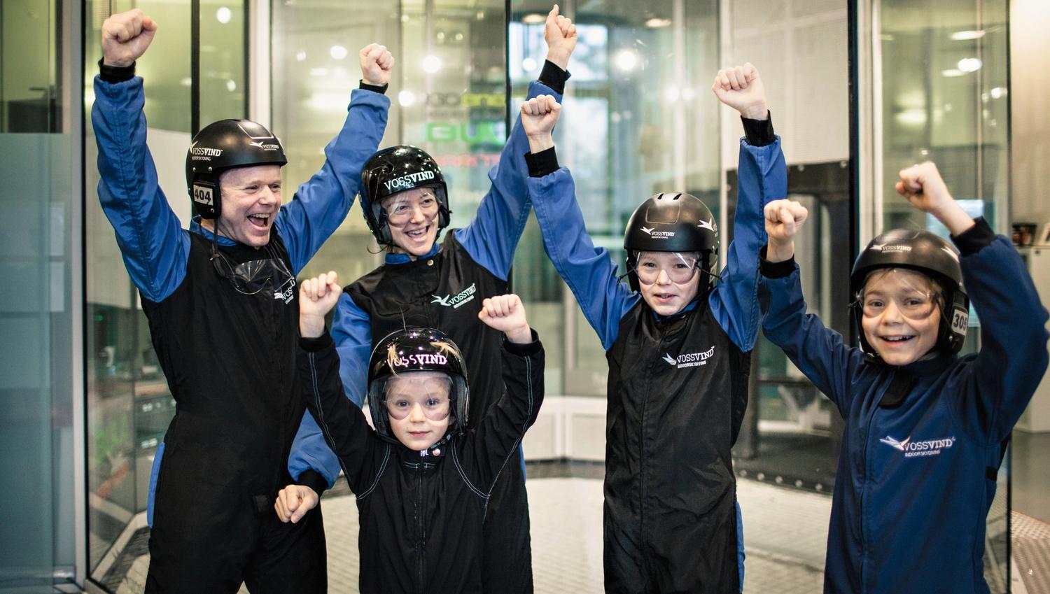Family celebrating after flying. Standing outside the wind tunnel in suits and helmets cheering with raised arms.